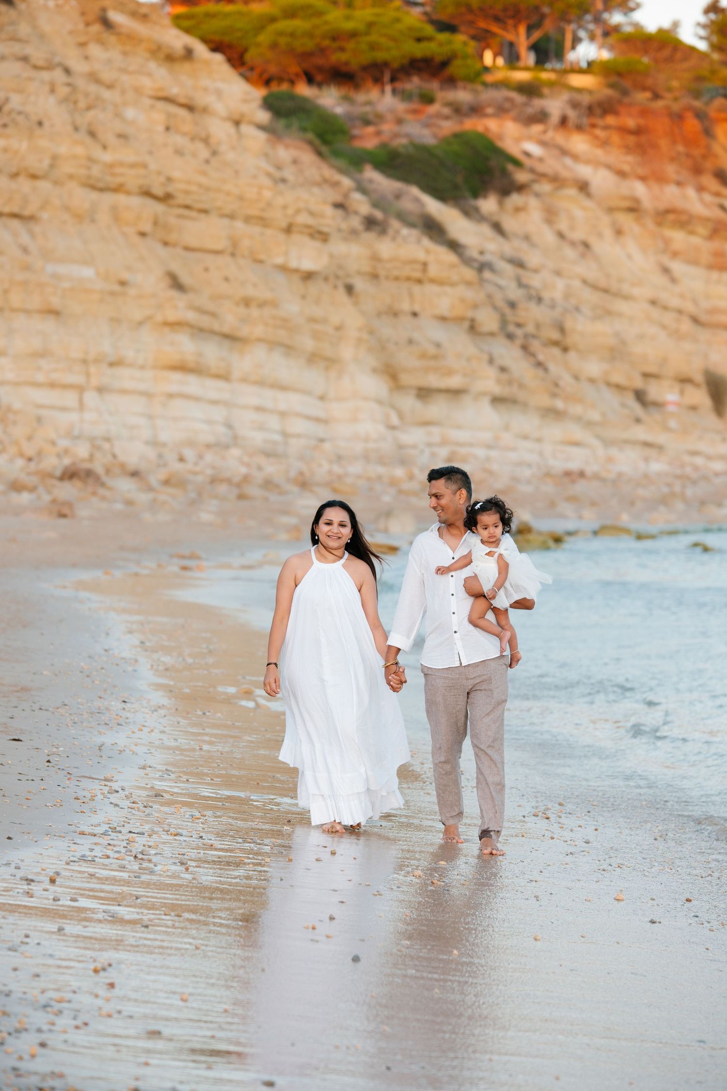 Family walking along shoreline holding their baby during first birthday session in Lagos Portugal