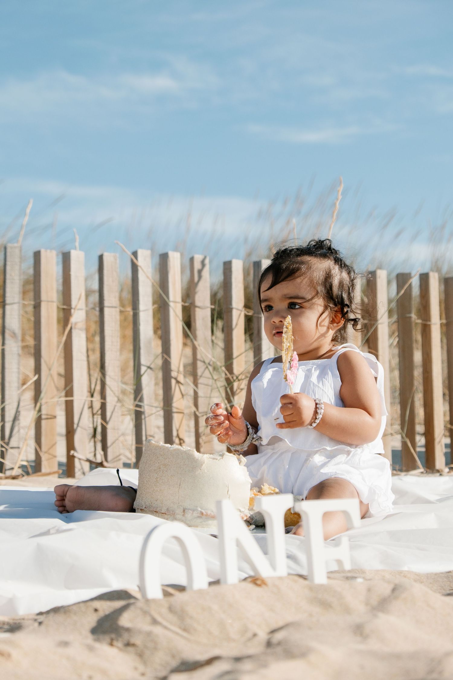Baby celebrating first birthday with cake cutting on sandy beach at Meia Praia.