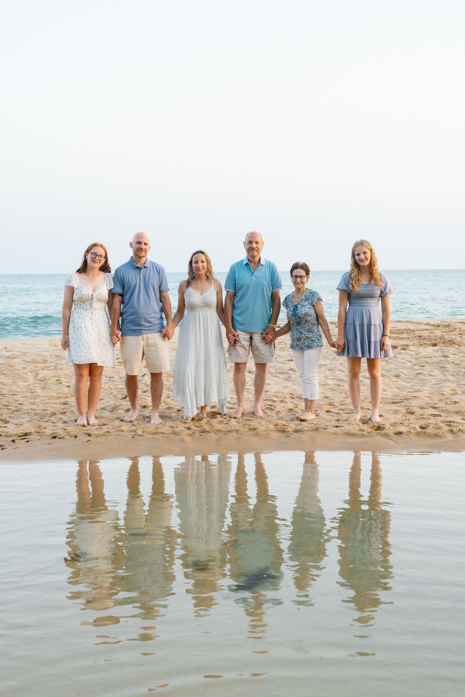 parents holding hands with children while reflections appear in wet sand at golden hour