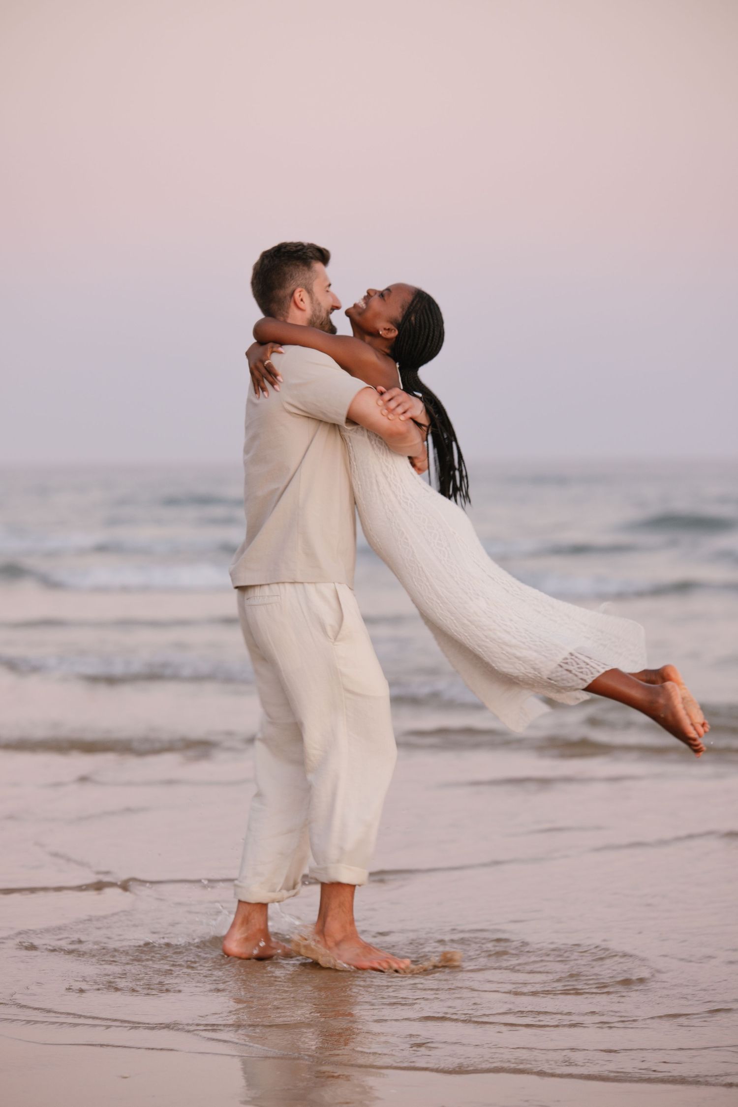 man twirling his girlfriend on the beach wearing white clothes