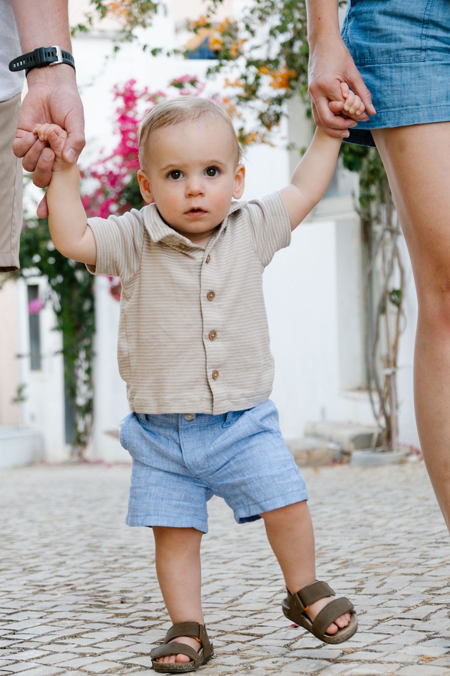 candid moment of toddler walking between parents in a colorful Portuguese alley with flowers in Lagos