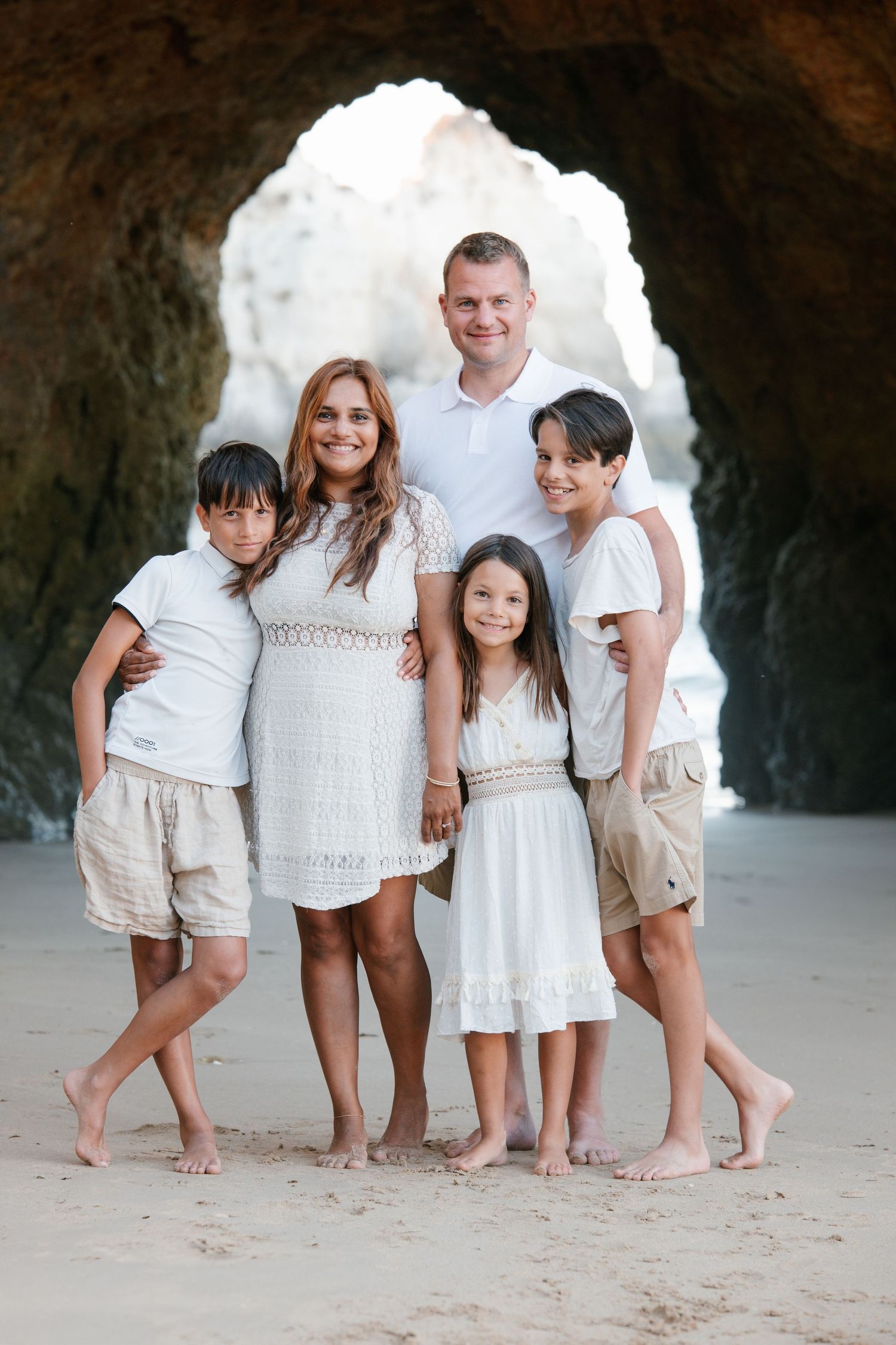 Family standing together under a rocky arch on the beach with ocean views behind them.