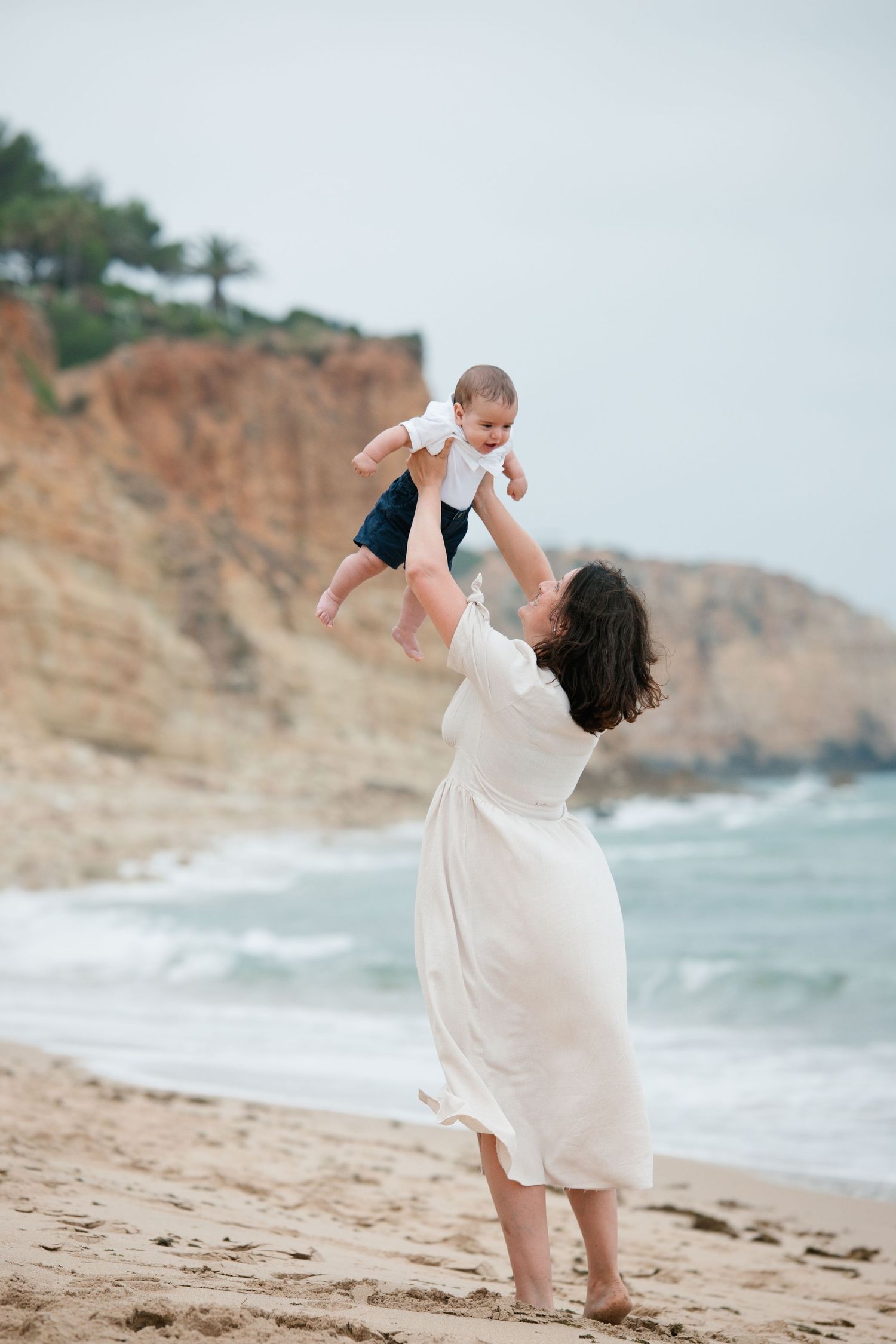Mom and baby playful moment on the beach with sunrise glow