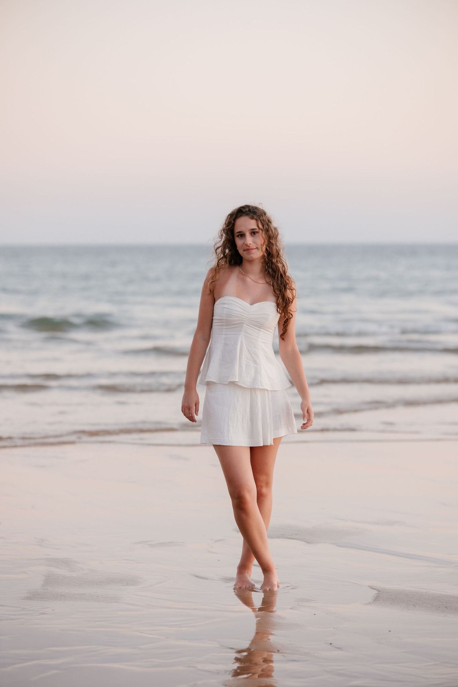 candit close-up beach portrait of girl in a white dress with sunset colors reflecting behind her
