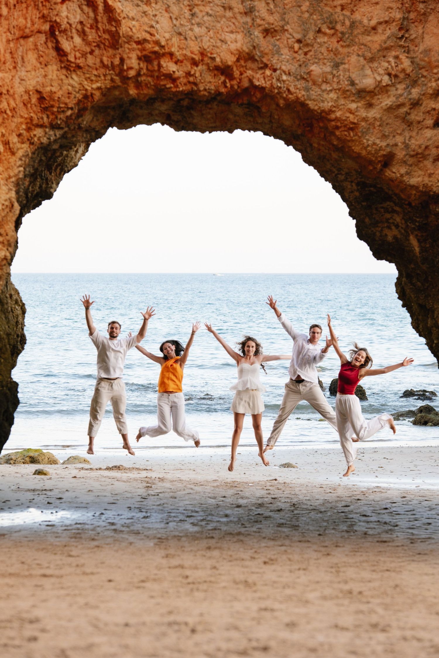 children jumping together under the natural rock arch at Praia Três Irmãos during sunset