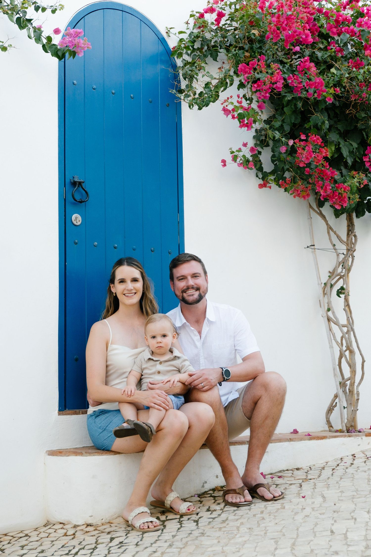 family sitting close together beside pastel blue door with blooming bougainvillea in a Portuguese street