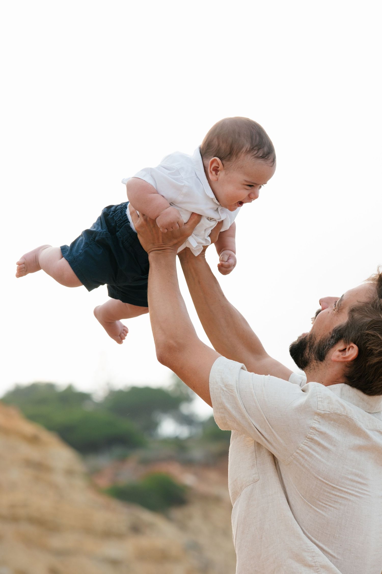 Dad lifting baby in the air on the beach at sunrise