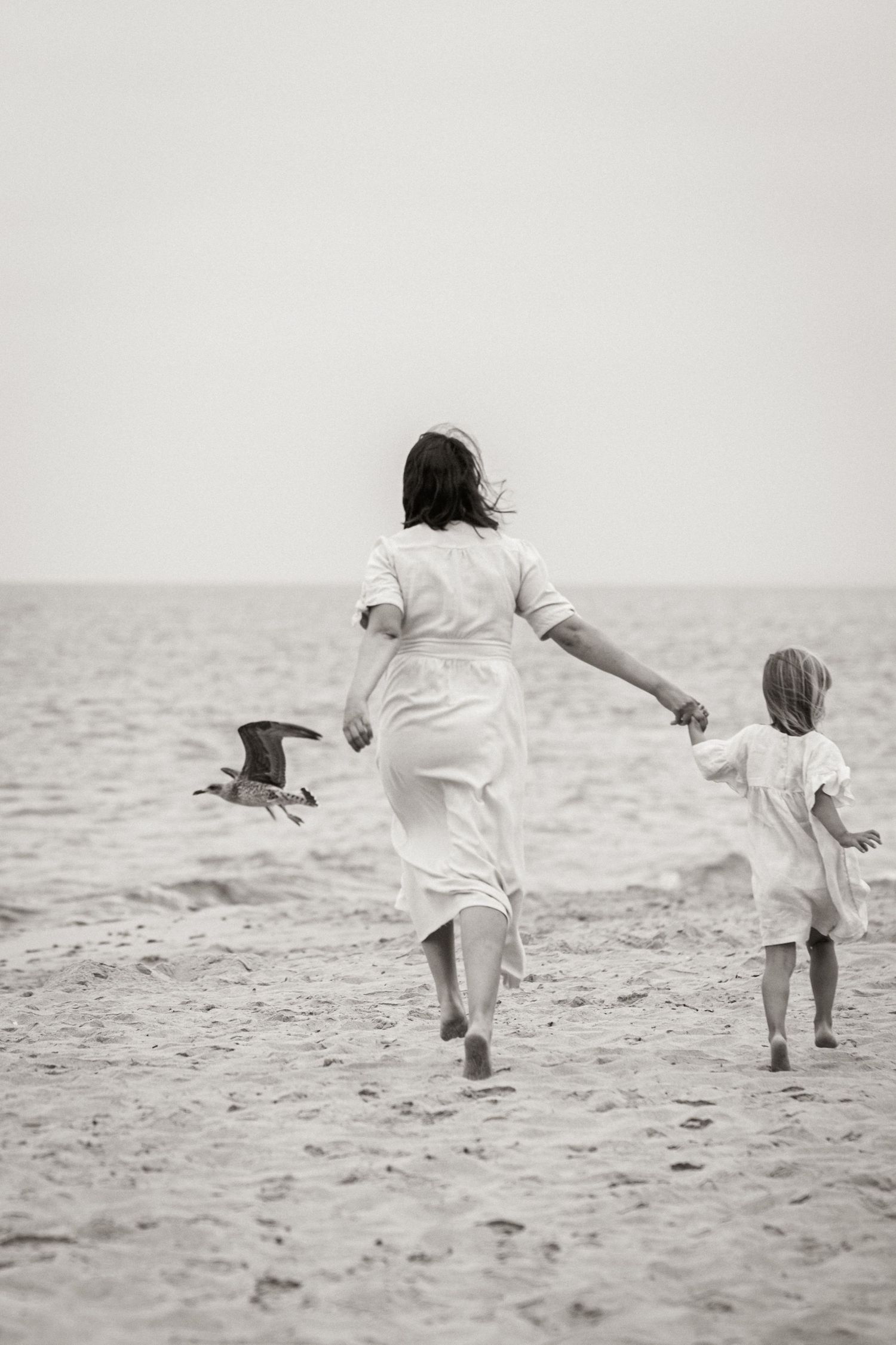 Mom and daughter running along the shoreline at sunrise on Porto Mós beach