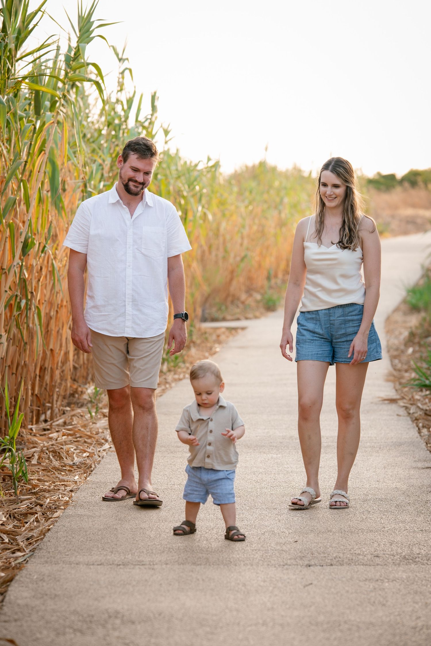 toddler leading the way on a paved path with parents smiling behind