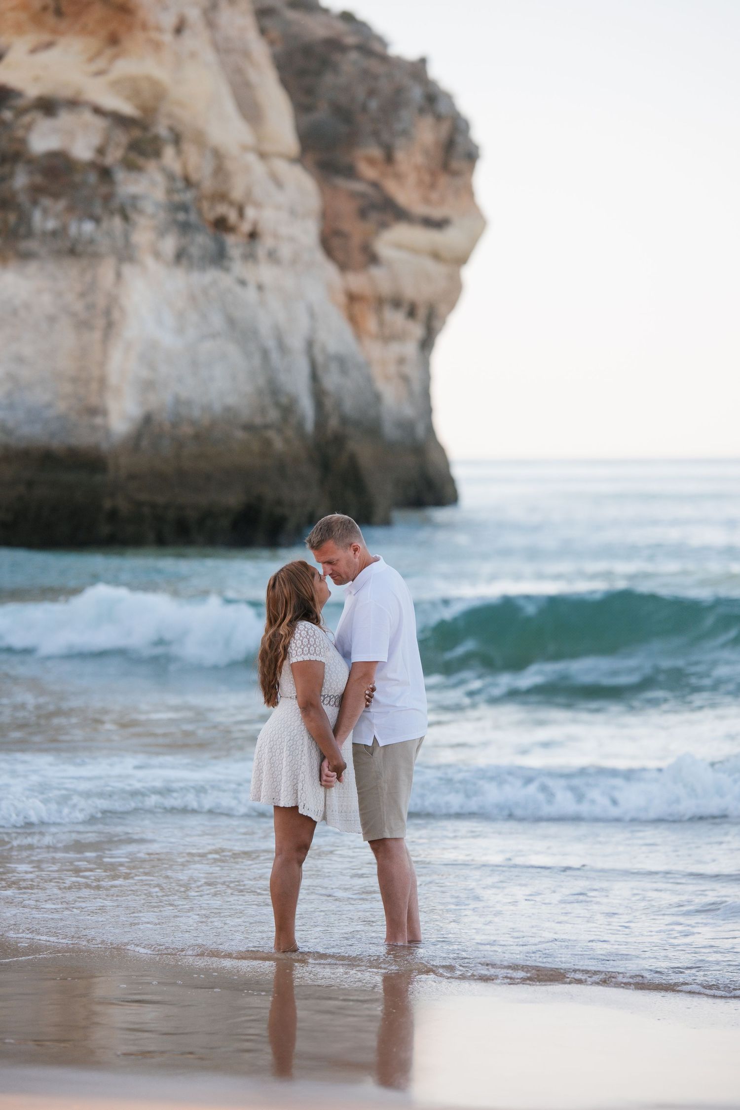 Parents holding each other on the beach in Alvor during sunset with waves behind them.