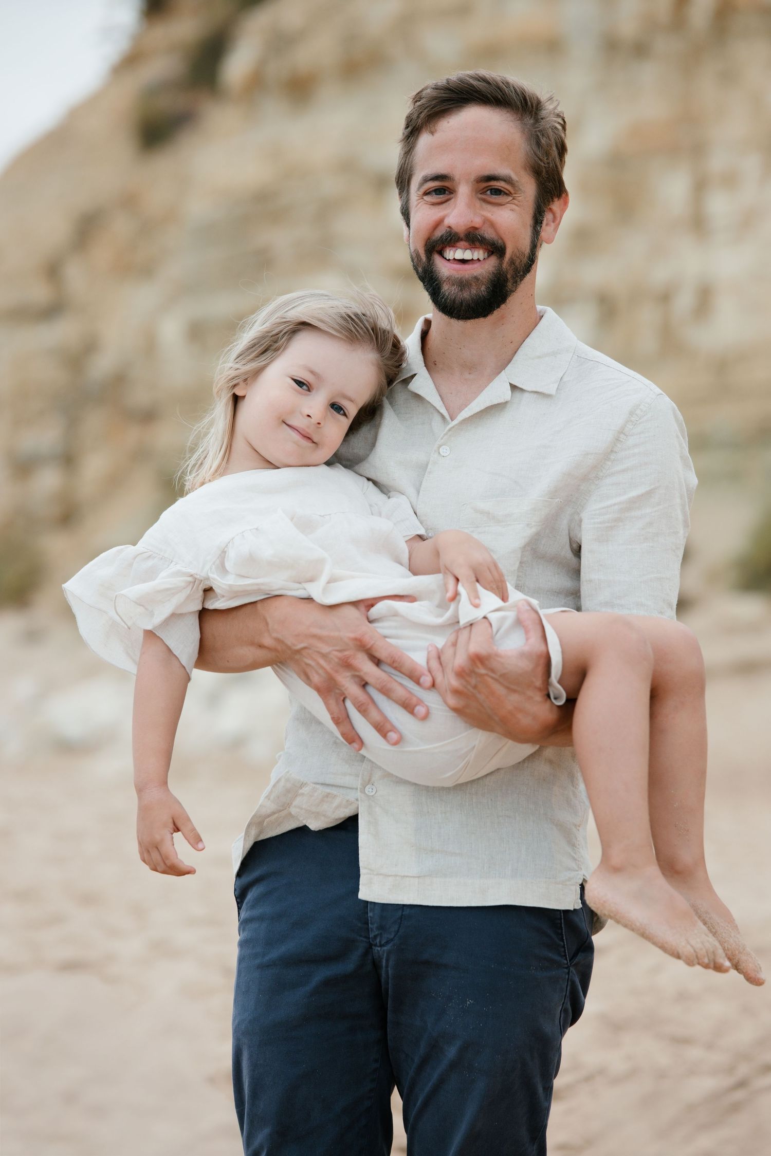 Dad holding daughter at sunrise on Porto Mós beach with cliffs in the background