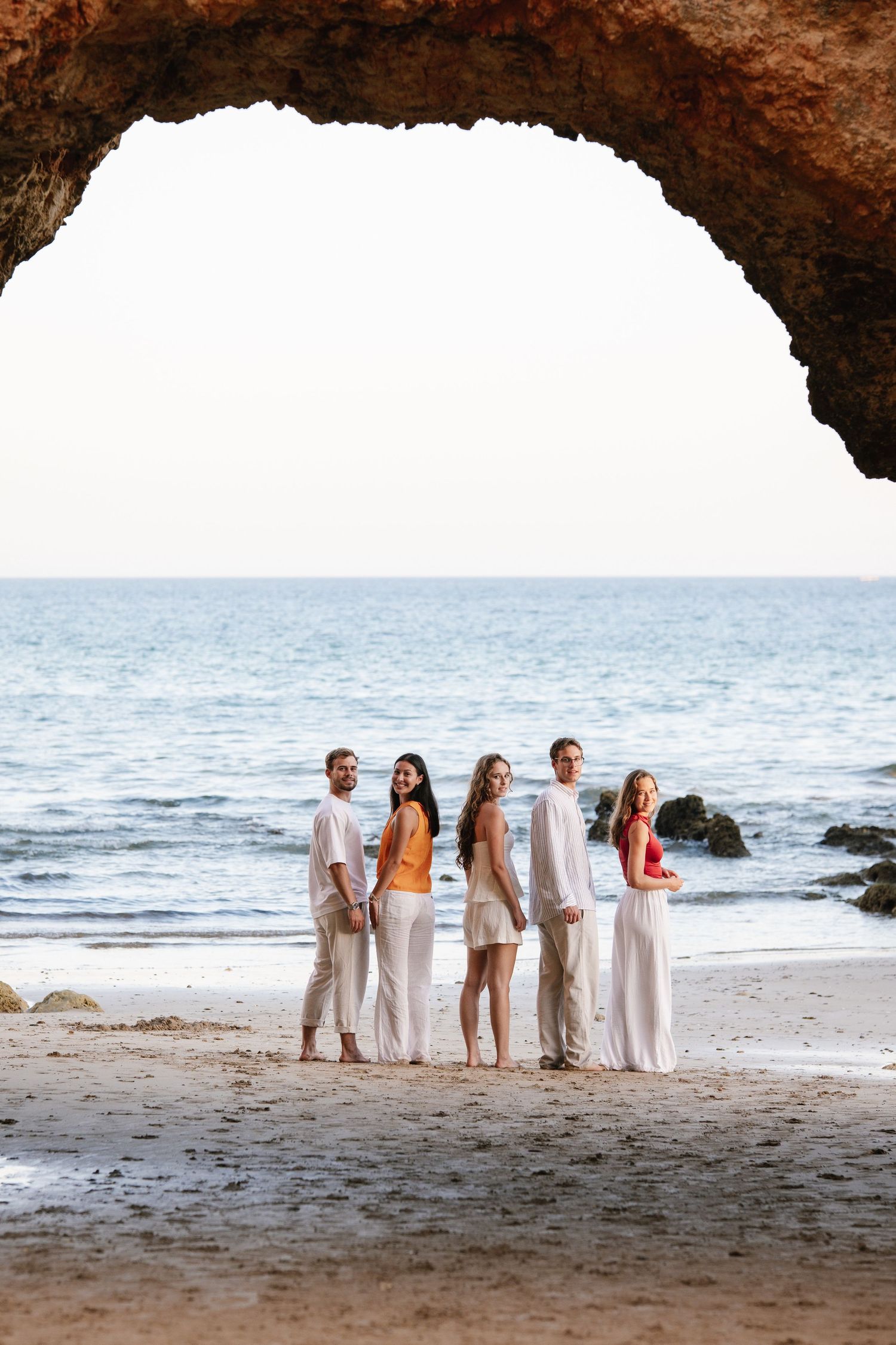 children standing under the rock arch at Praia Três Irmãos looking at the camera and smiling