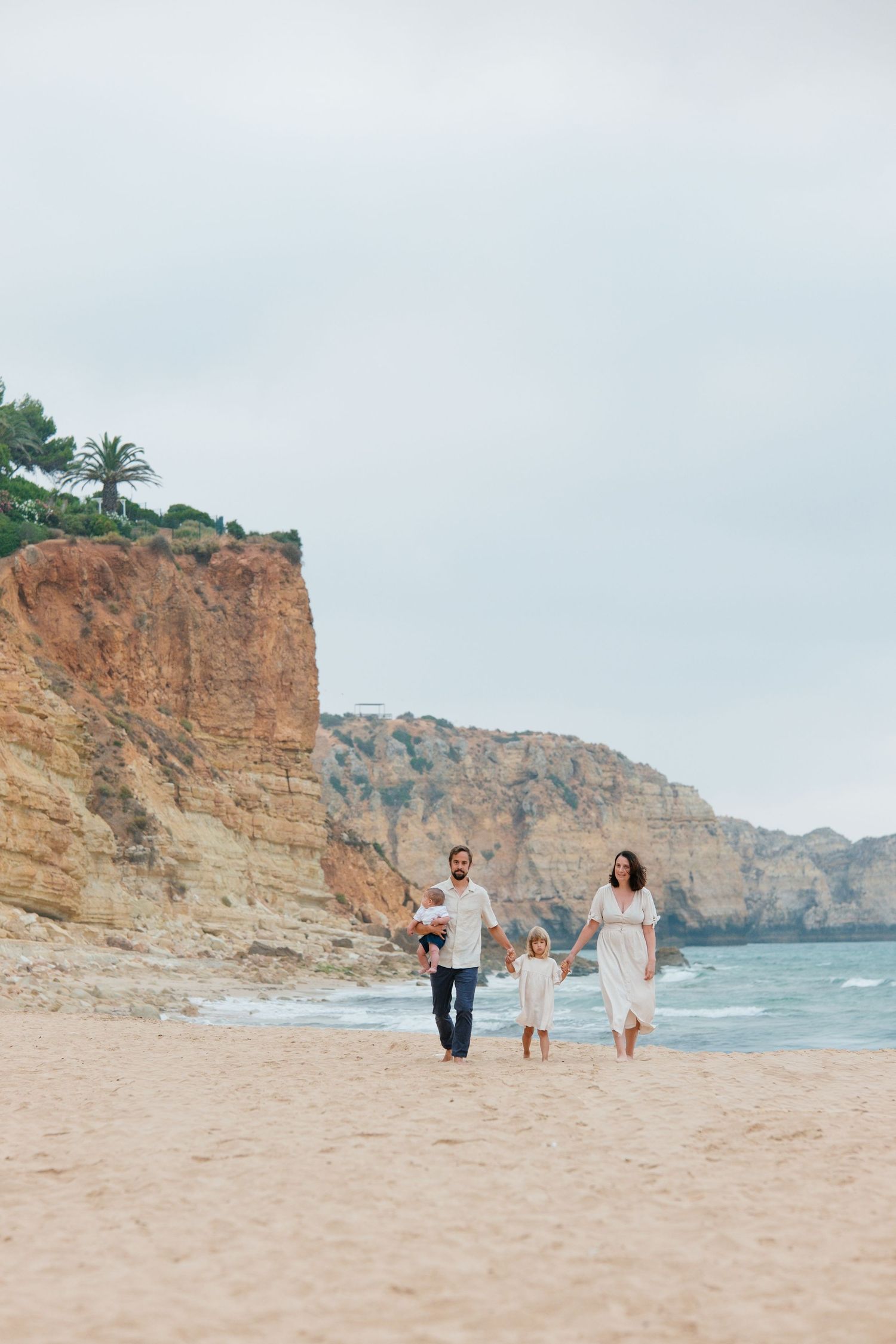 Family walking along the shoreline with the Porto Mós cliffs in the background at sunrise — Lagos family photographer.