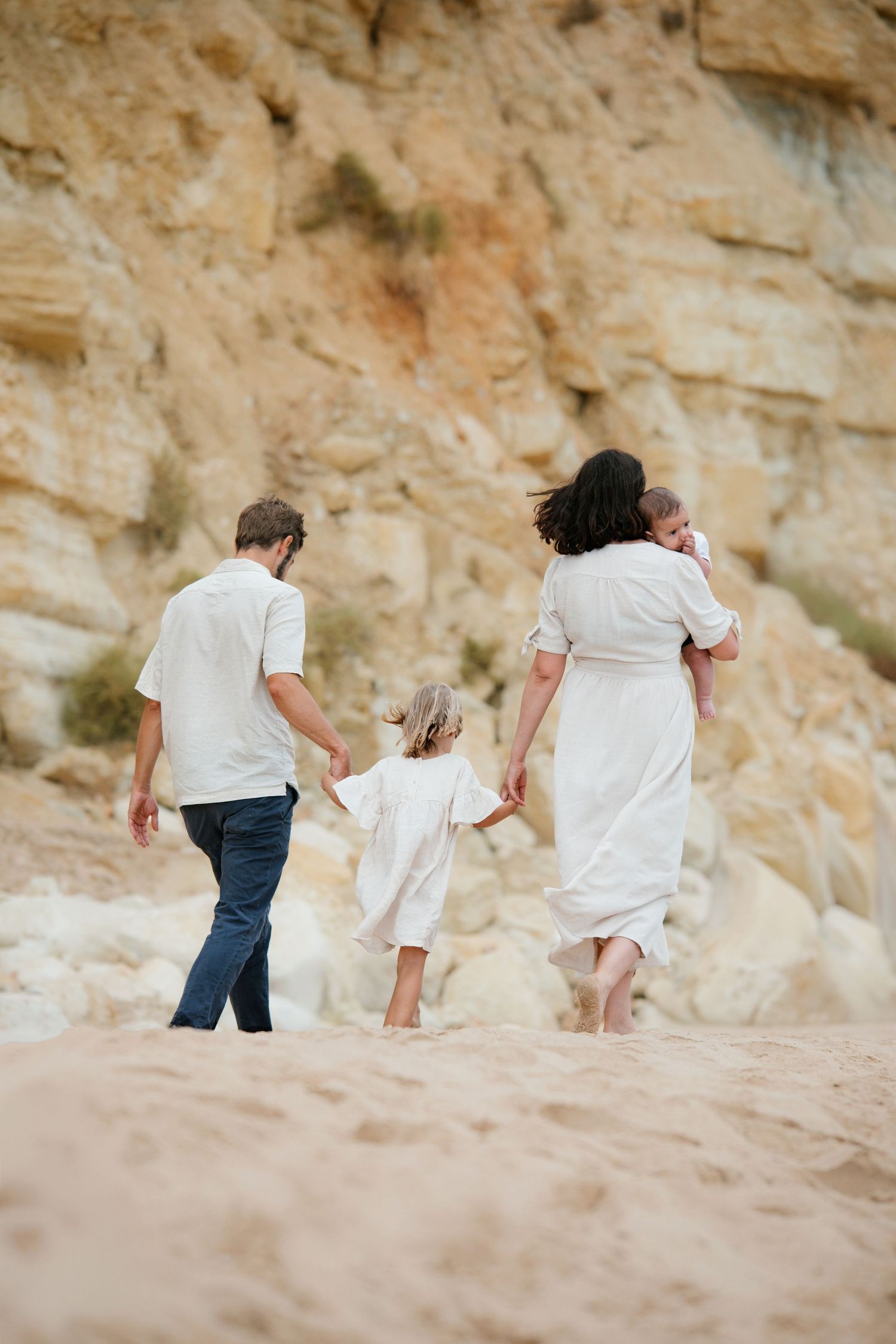 Family walking along Porto Mós beach at sunrise with gentle waves — Lagos family photographer.