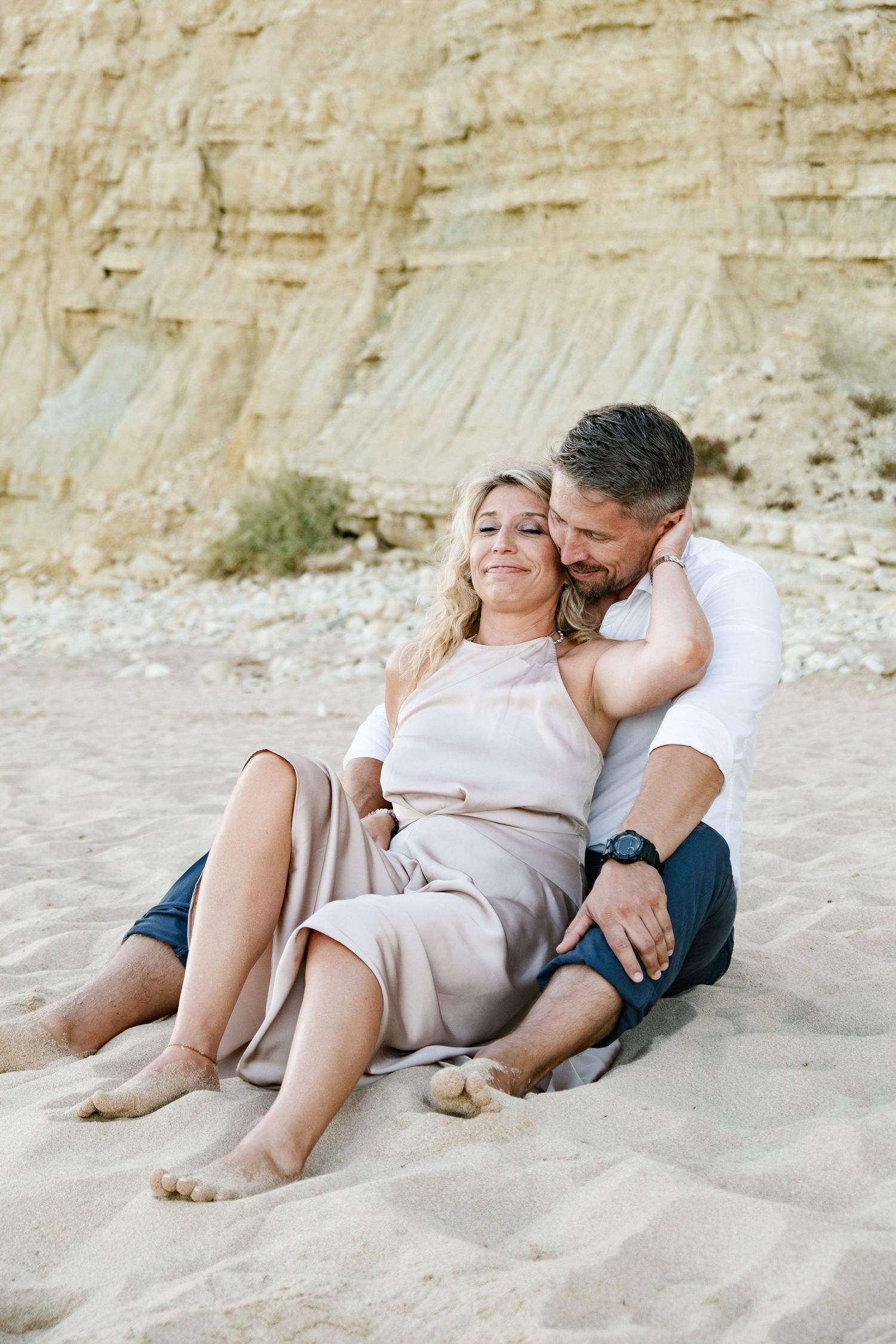 Couple sitting close on the beach with soft sunset light.