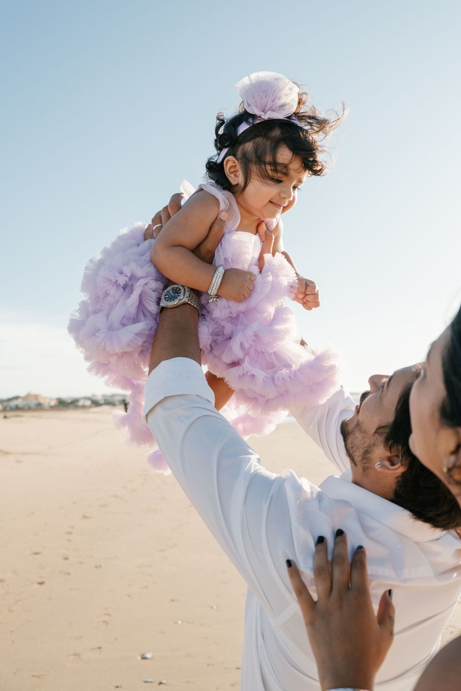 Parents lifting baby into the air on the beach with soft golden light at Meia Praia.