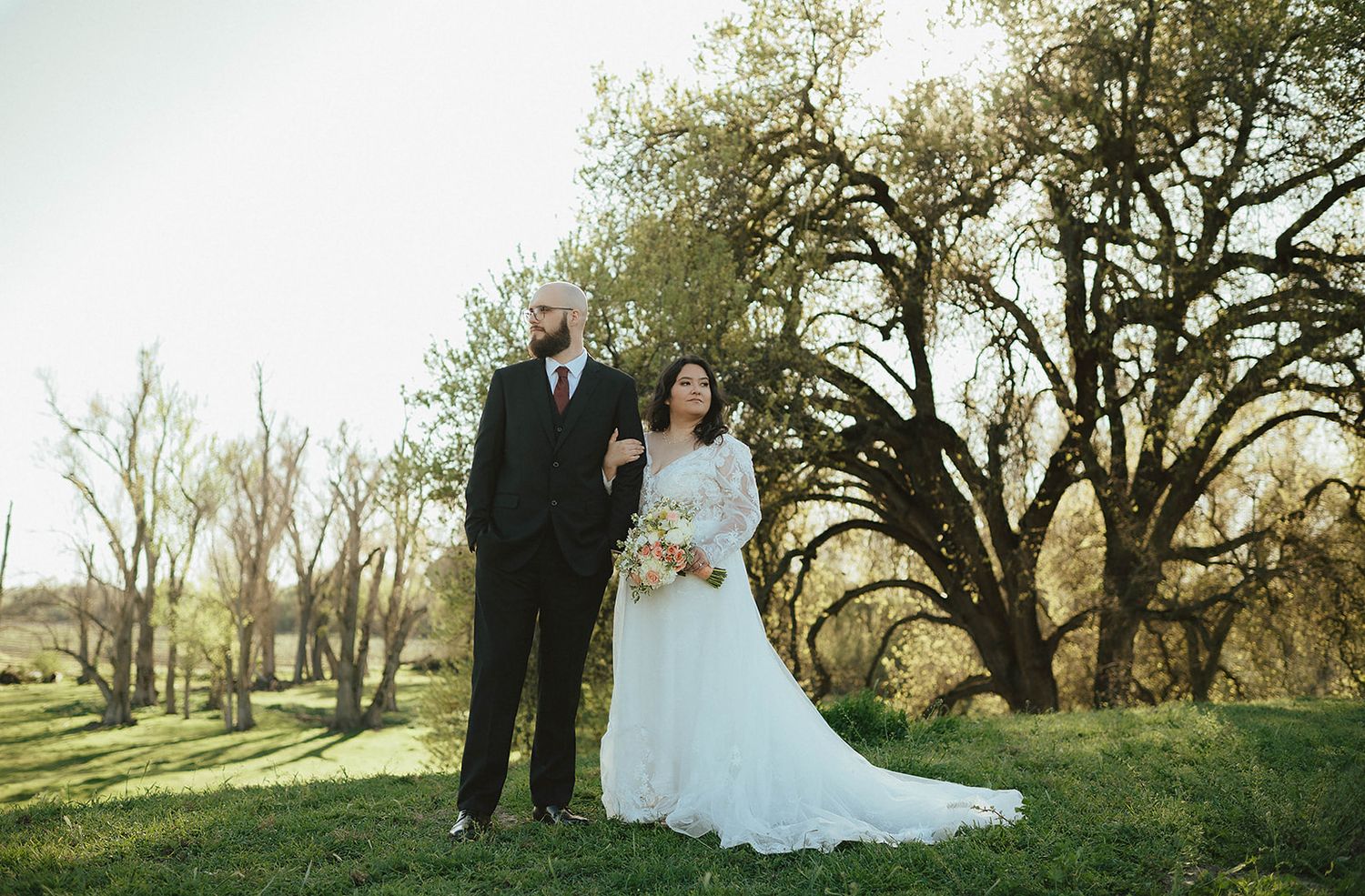 elopement session bride and groom starring opposite sides in a green field full of green trees in Sanger California