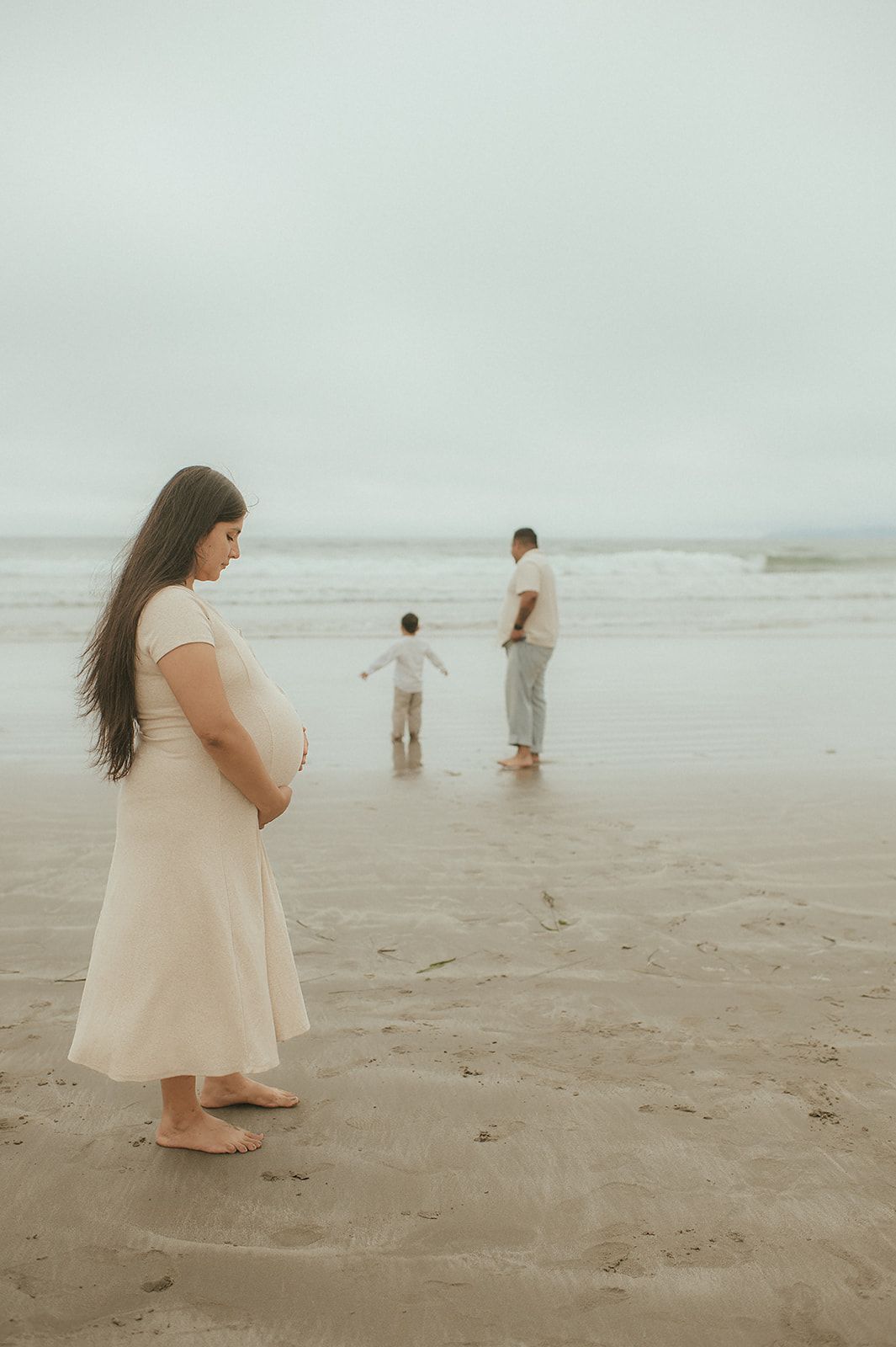 morro rock california maternity family session mother looking down at her belly in her cream dress