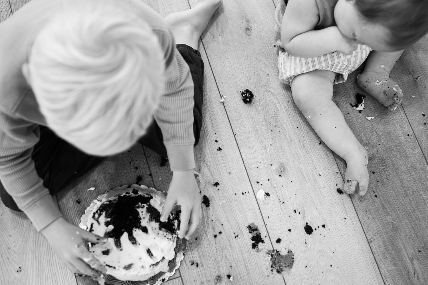 Overhead view of siblings smashing cake on wood floor. Black and white milestone session in Columbus.