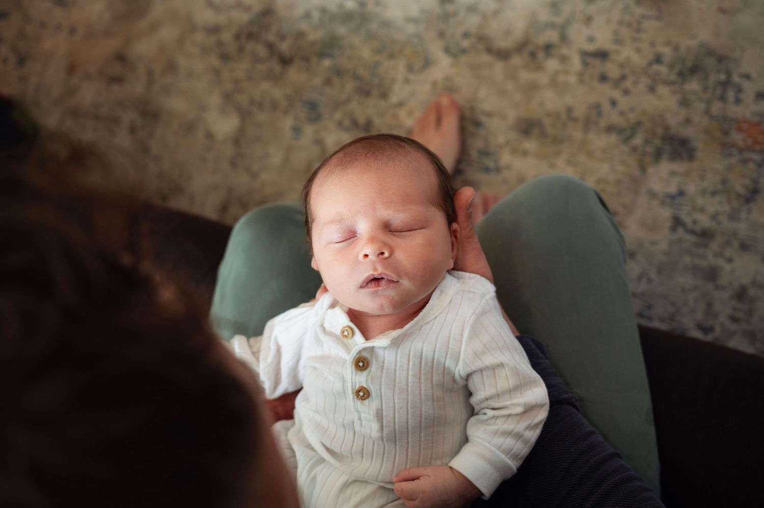 In-home newborn photography in Worthington, Ohio, featuring a peaceful baby resting in parent’s lap with natural light.