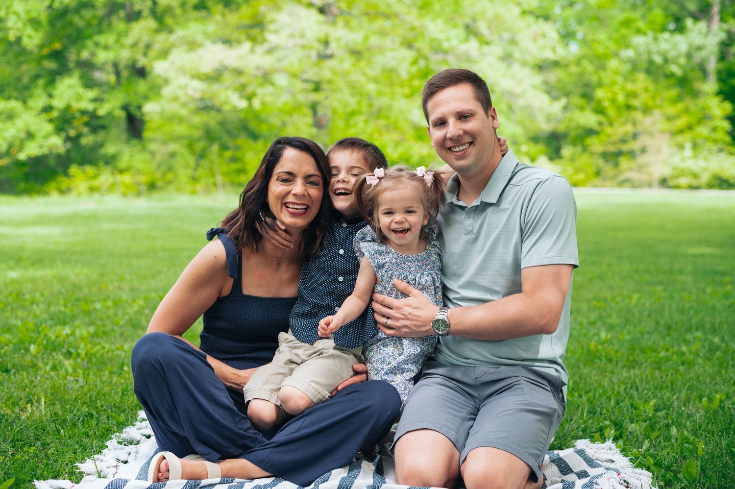 Family of four laughing together on picnic blanket in open field at Highbanks Metro Park