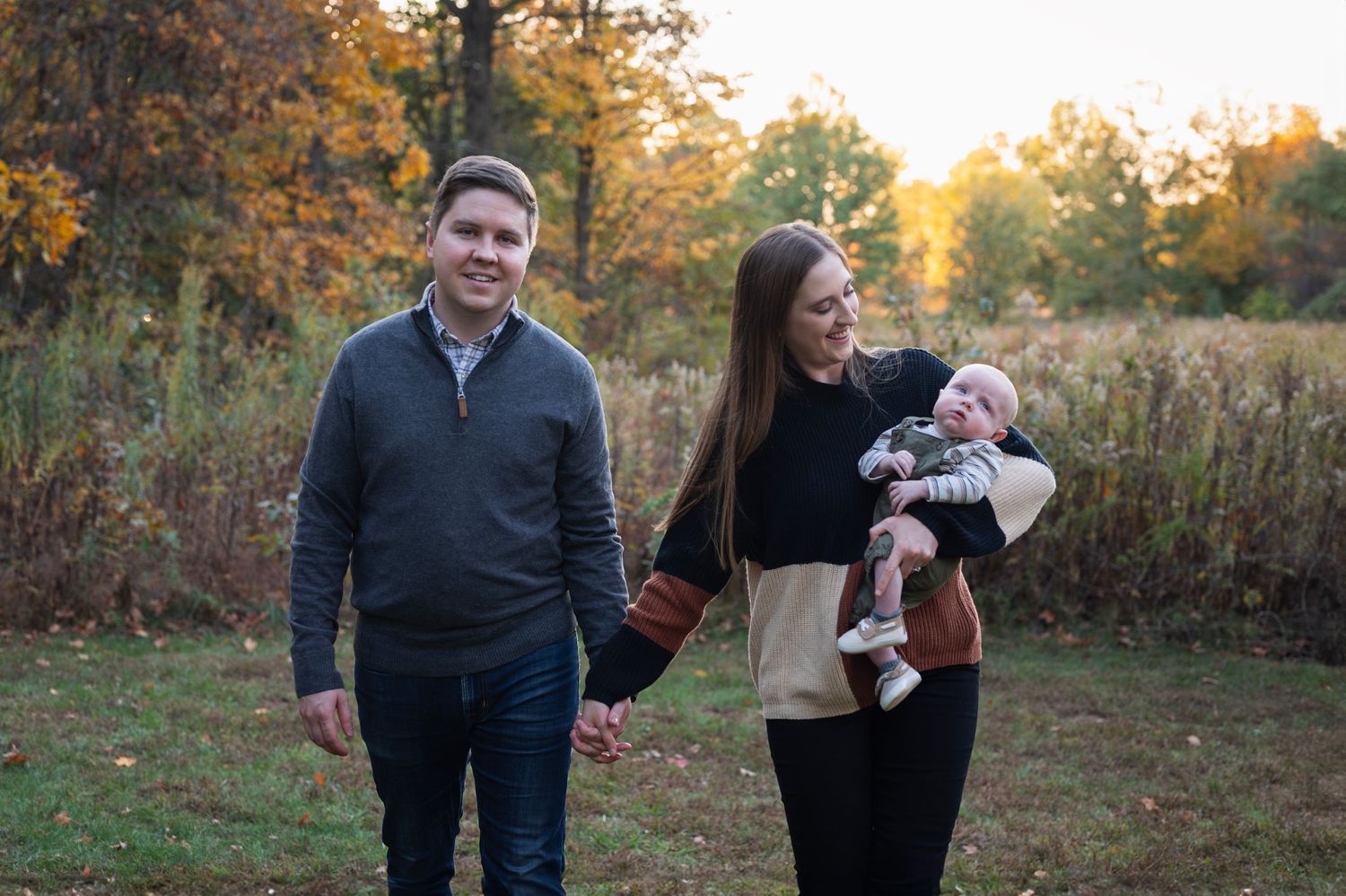 Mom and dad walking with newborn in fall field at Highbanks Metro Park in Lewis Center