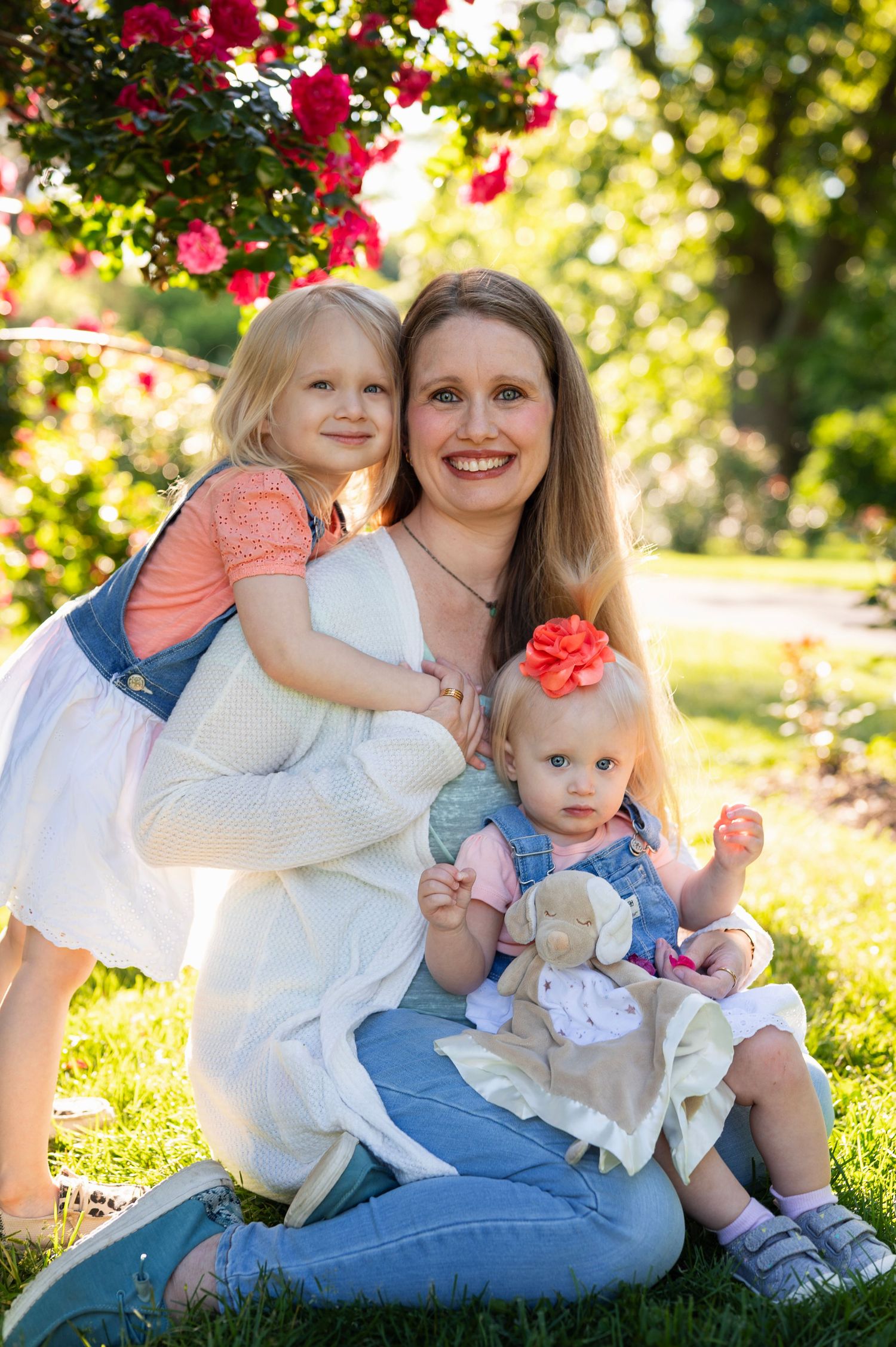 Mom with two young daughters sitting under blooming roses at Park of Roses family session.