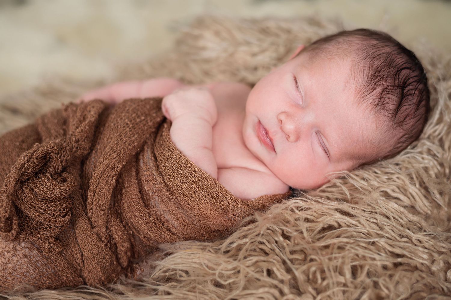 Newborn wrapped in brown blanket sleeping on faux fur—studio session by Boundless Joy Photography