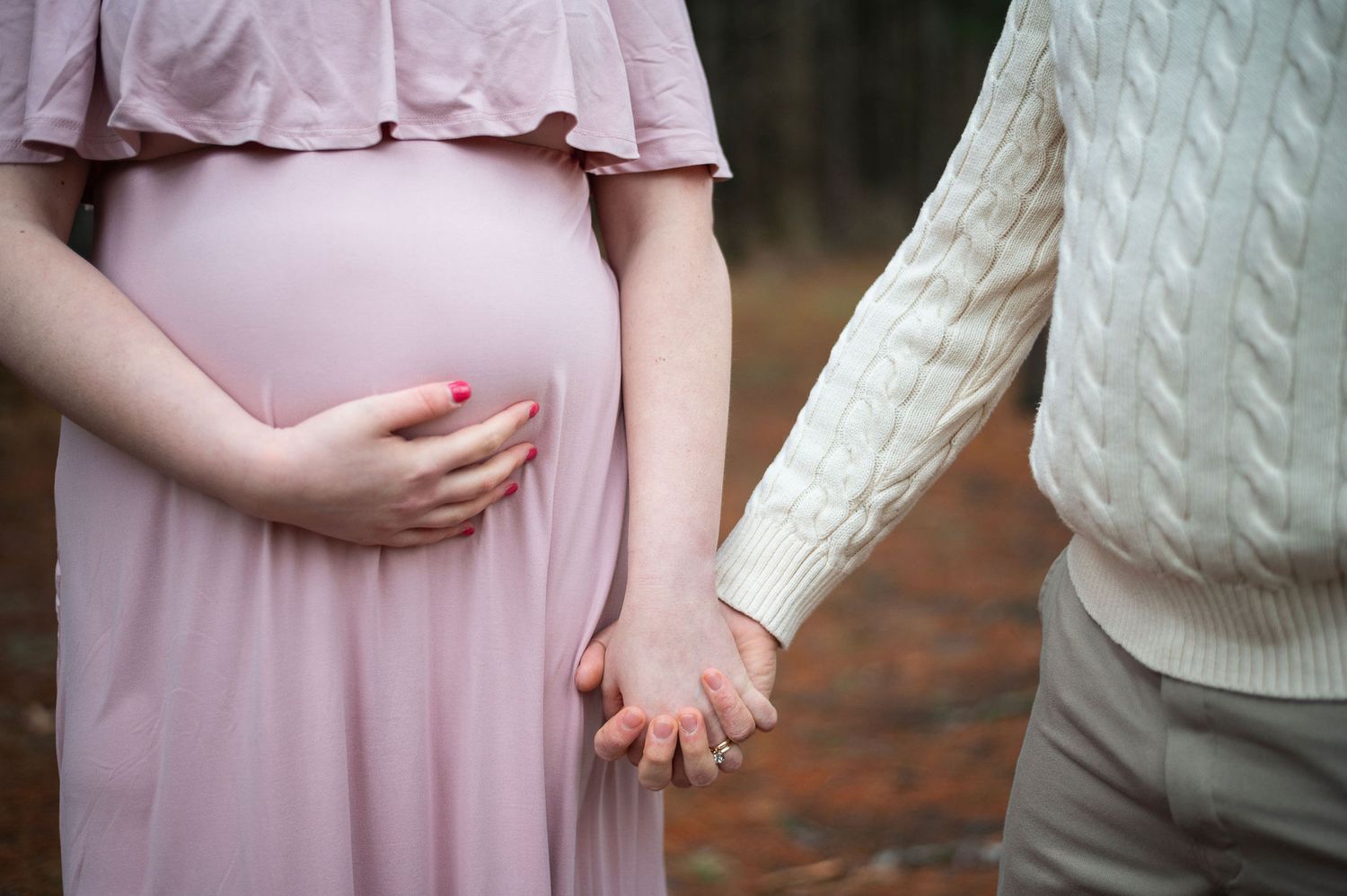 Close-up of maternity session showing baby bump and couple holding hands in soft outdoor light.