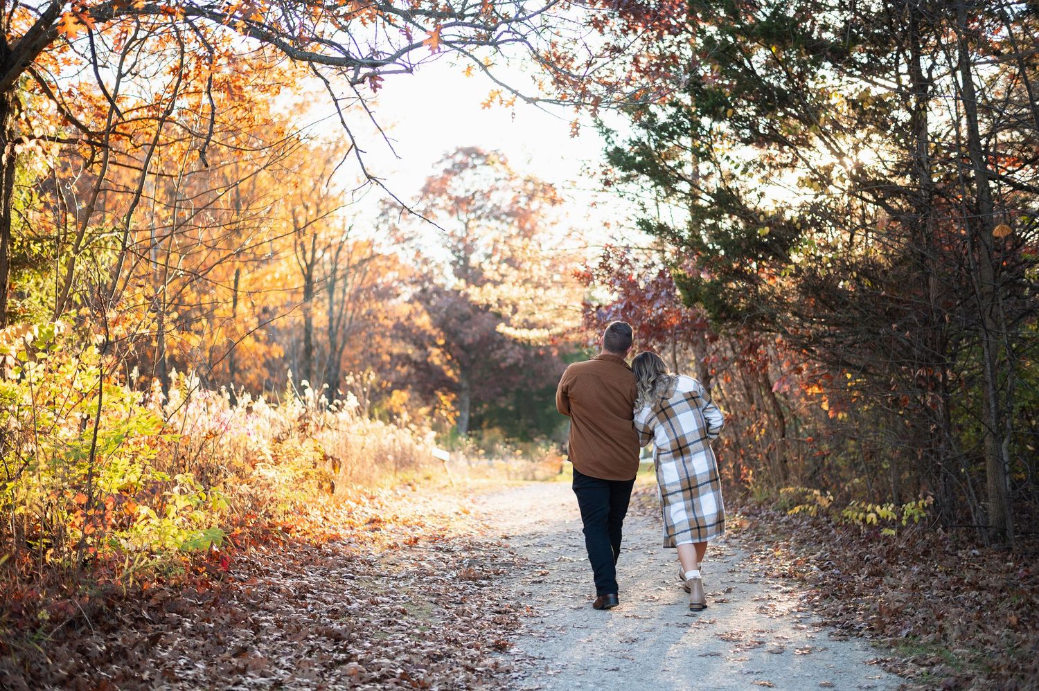 Couple walking arm in arm down a wooded trail surrounded by glowing fall leaves. Highbanks Metro Park