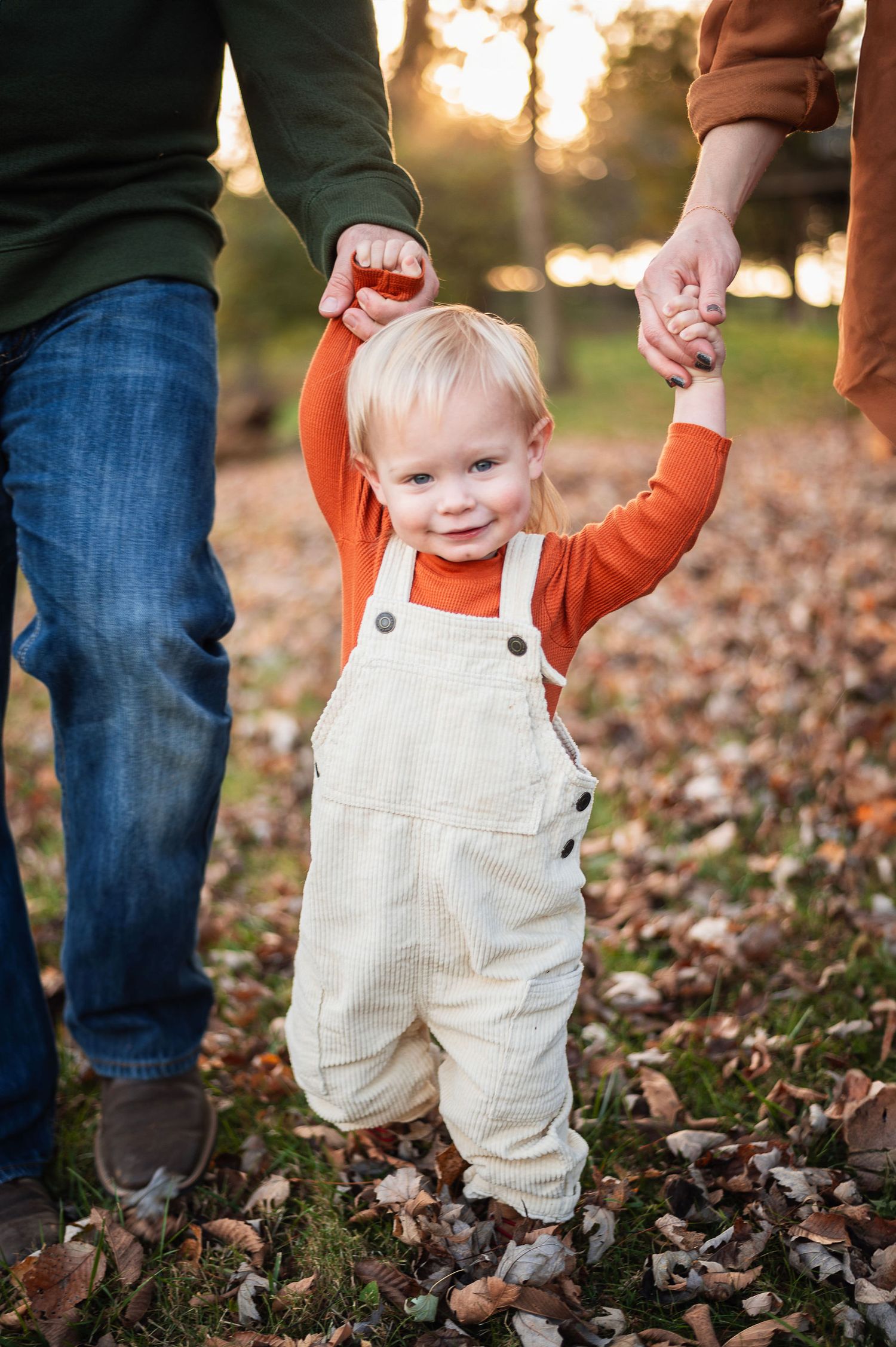 Toddler walking hand-in-hand with parents during a fall session at Highbanks Metro Park.