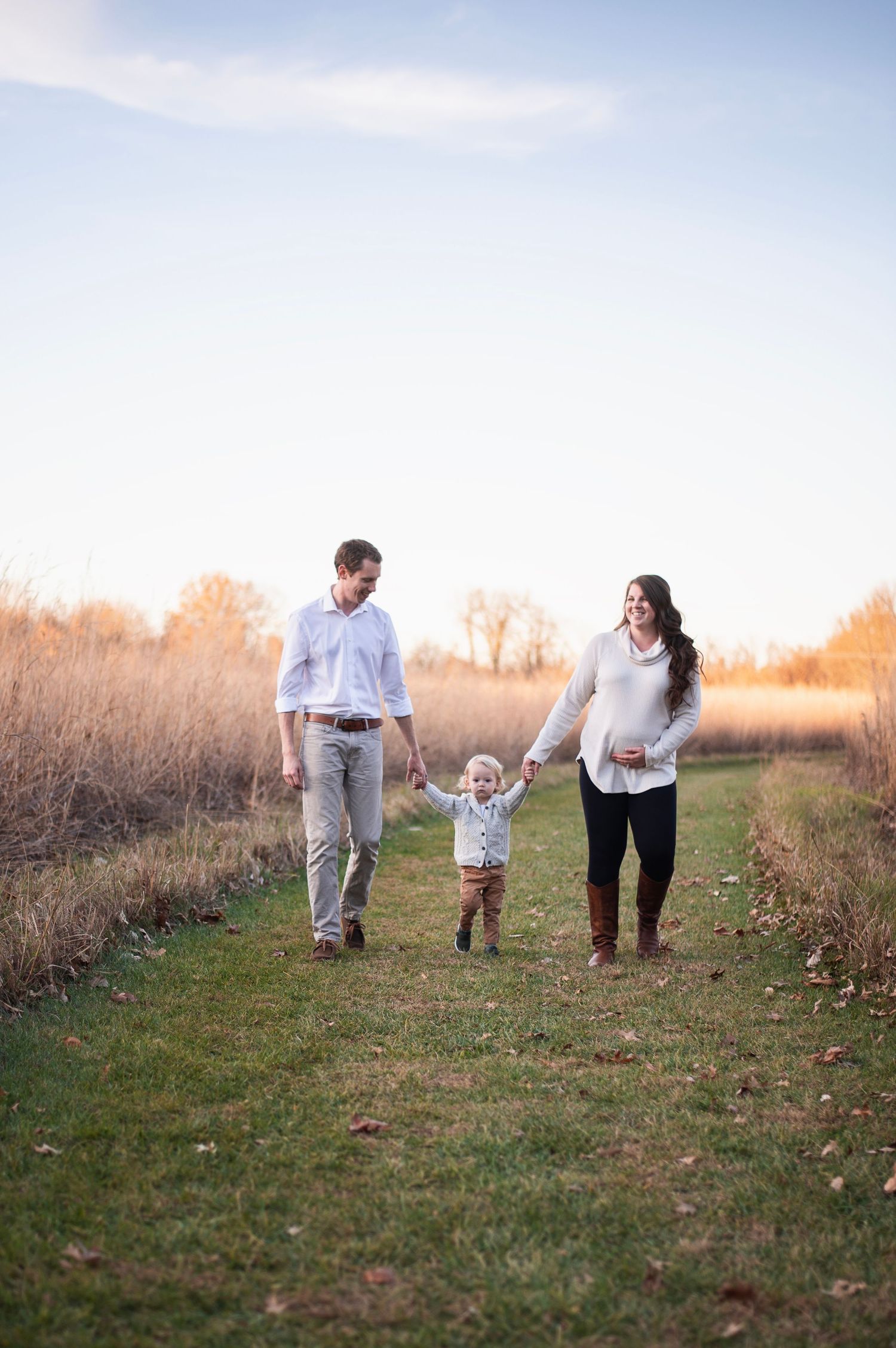 Parents lifting toddler between them while walking in tall grass field at Rocky Fork Metro Park.