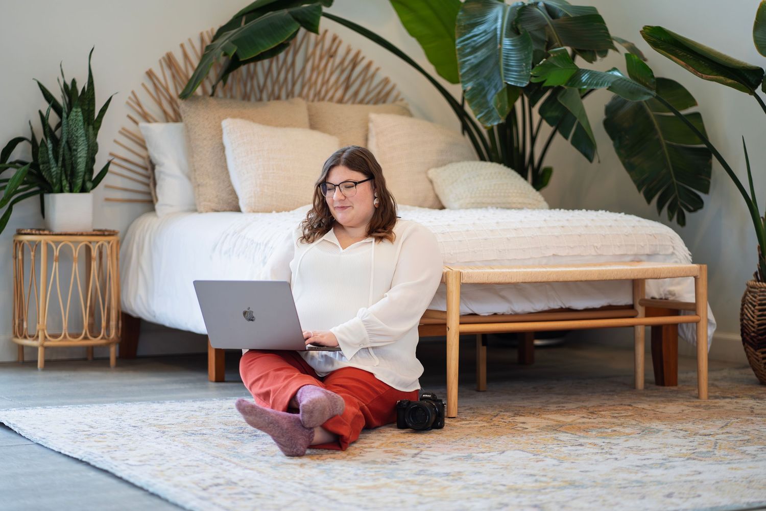 Photographer sitting on bedroom floor with laptop and camera, editing client photo gallery.