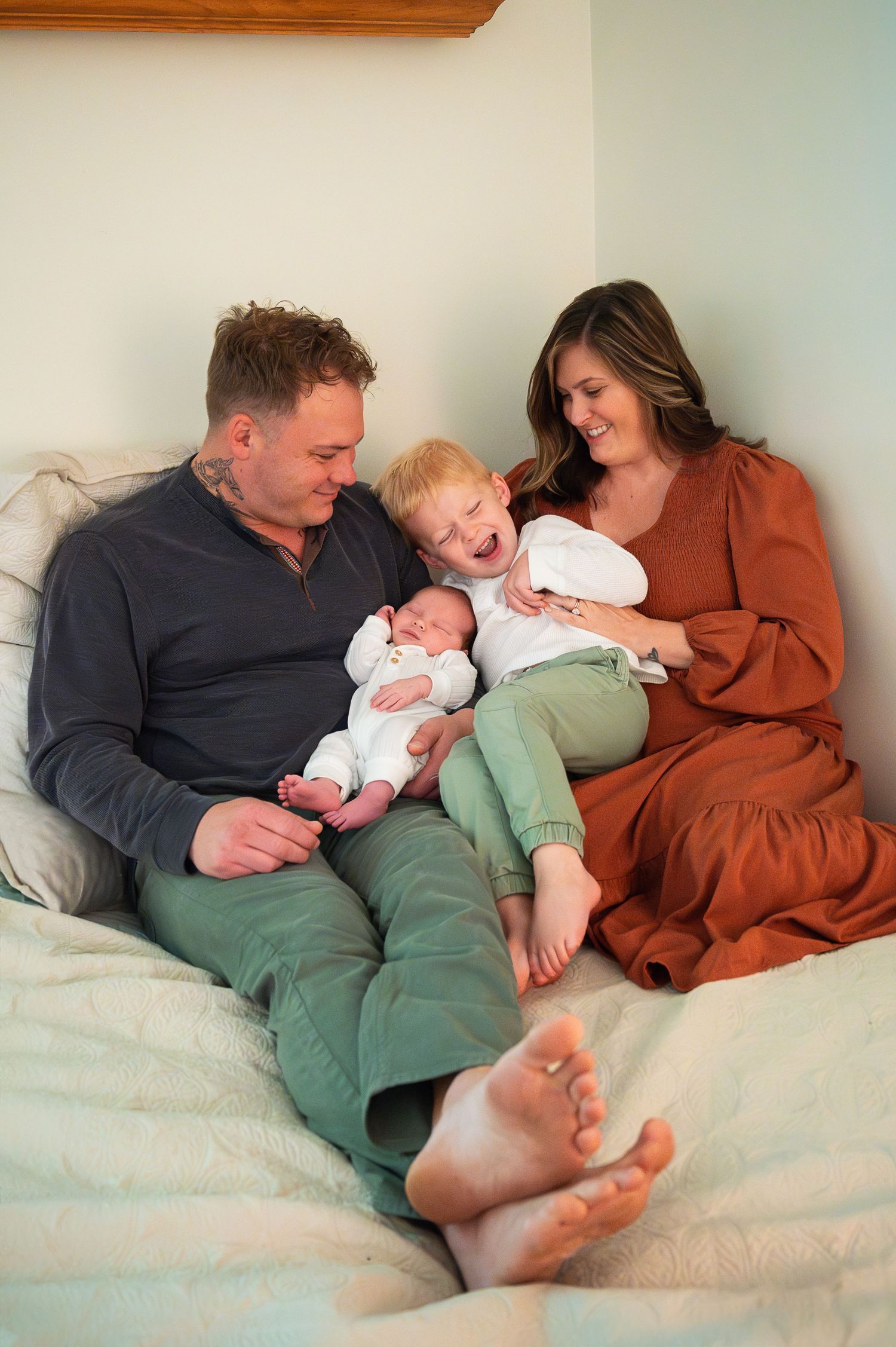 Big brother giggles while holding baby sister close in bed during a lifestyle family photo session at home.