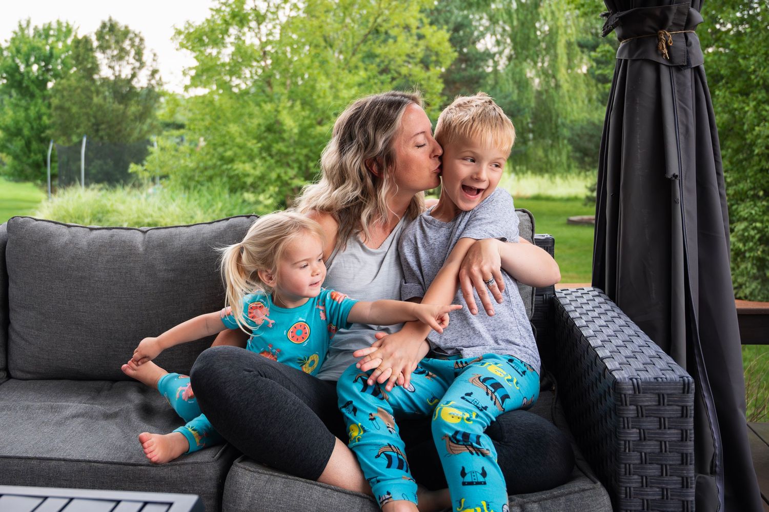 Mom cuddles and kisses her two giggling kids in pajamas during a playful in-home photo session.