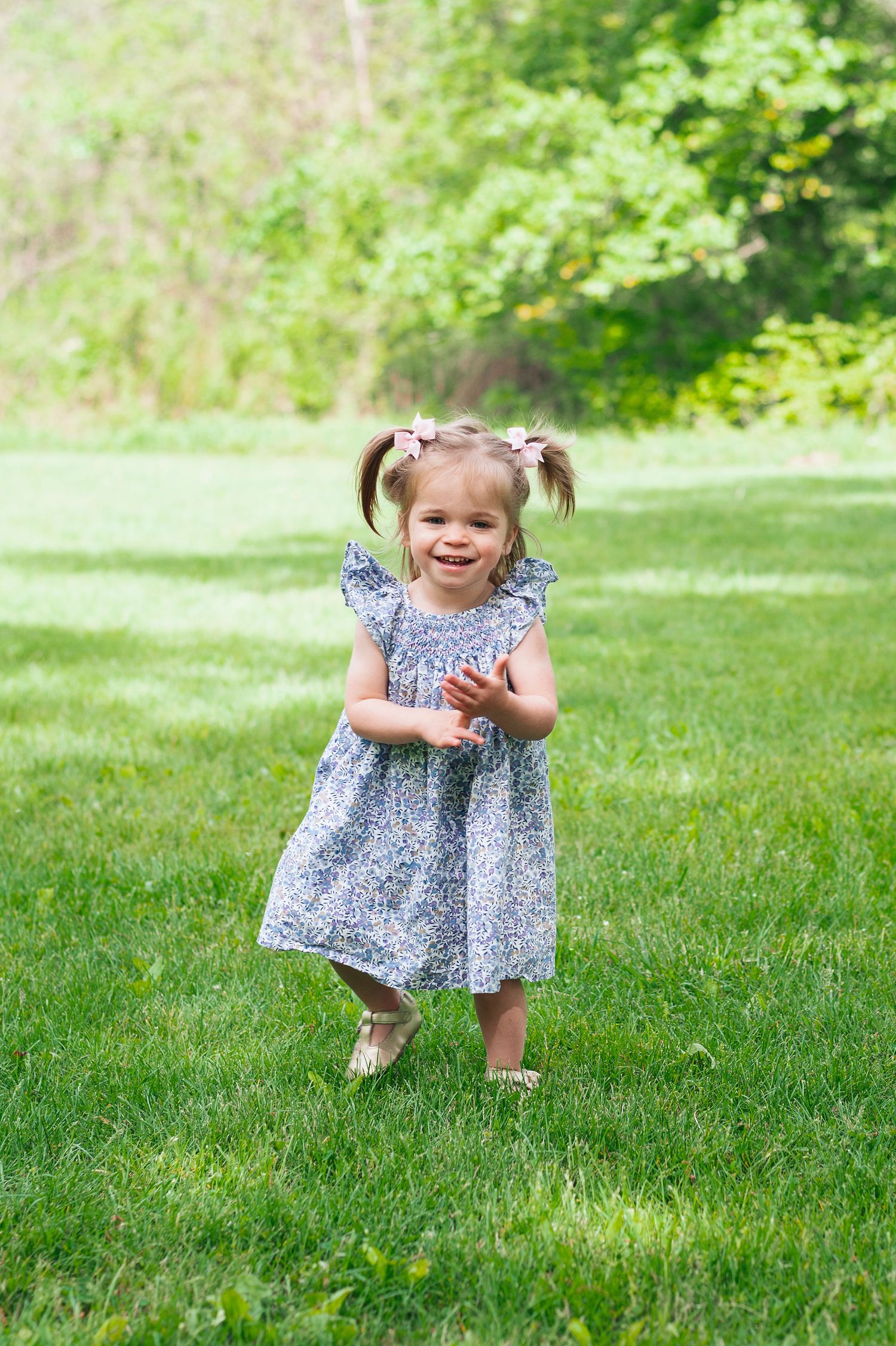 Little girl clapping and smiling in a sunlit field during a milestone session at Highbanks Metro Park in Columbus, Ohio.