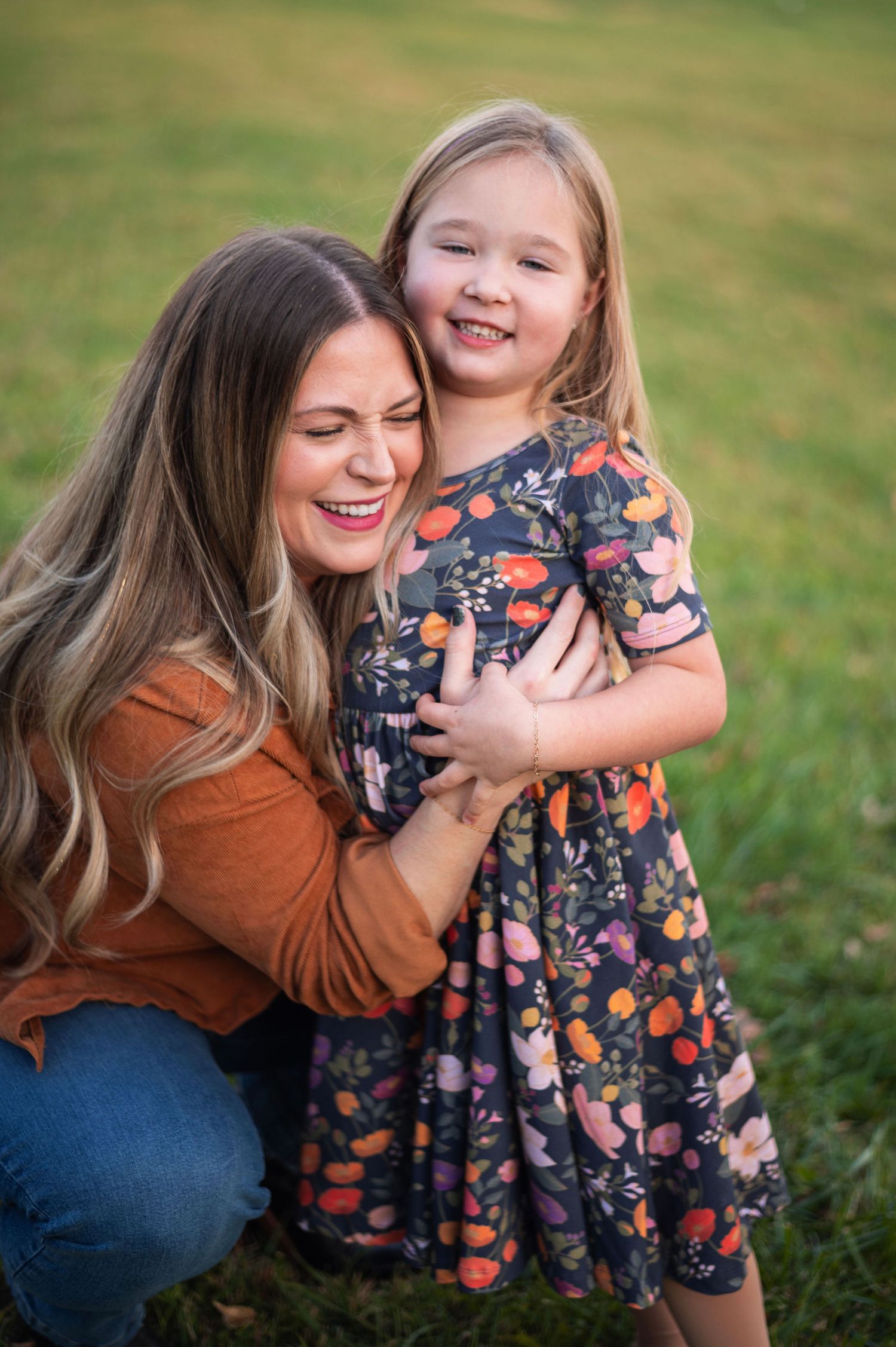 A mama laughs while hugging her daughter in a colorful dress during golden hour family photos in Westerville.