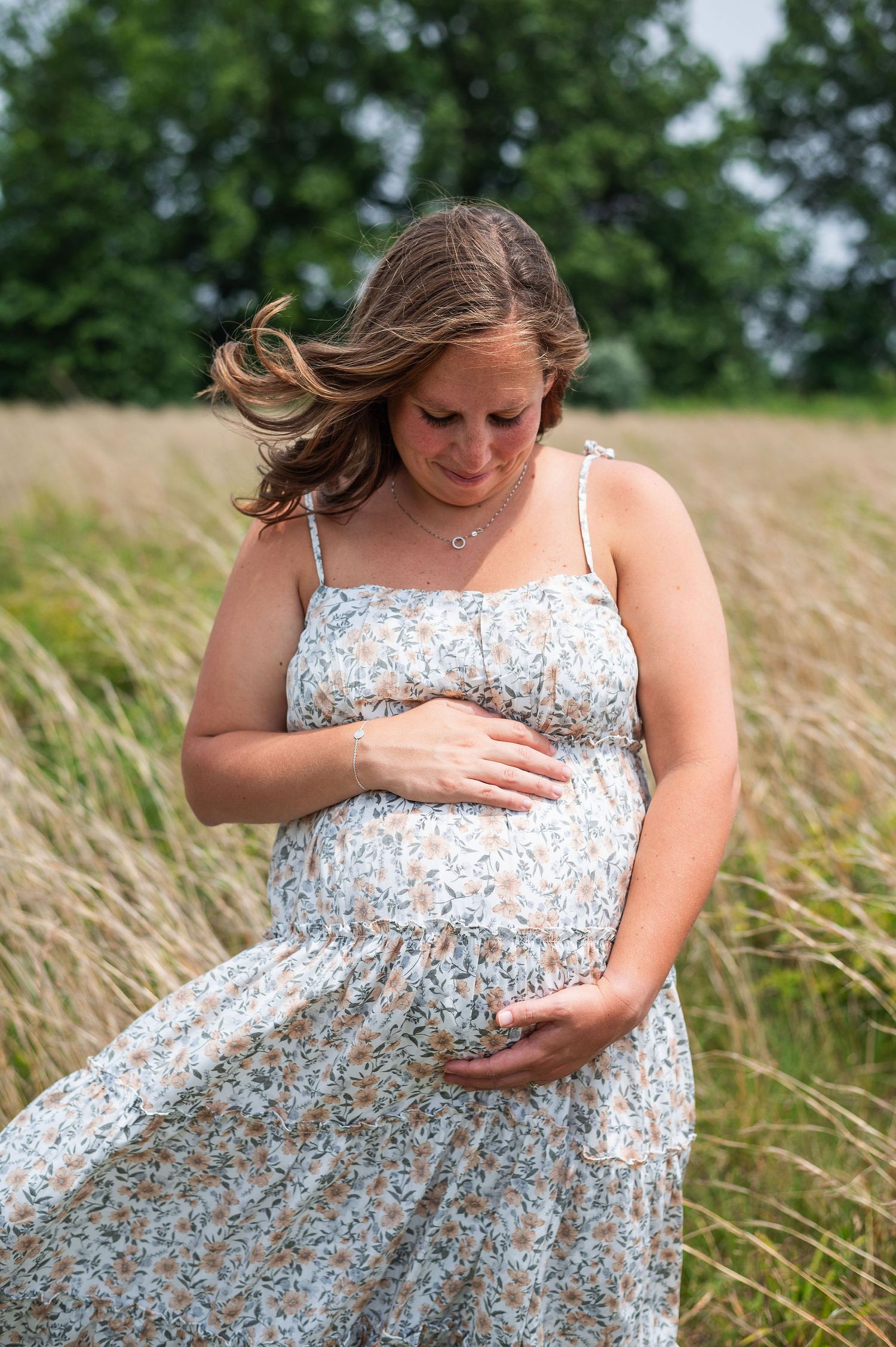 Pregnant woman holding her belly in a floral dress during a maternity session at Rocky Fork Metro Park in Columbus, Ohio.