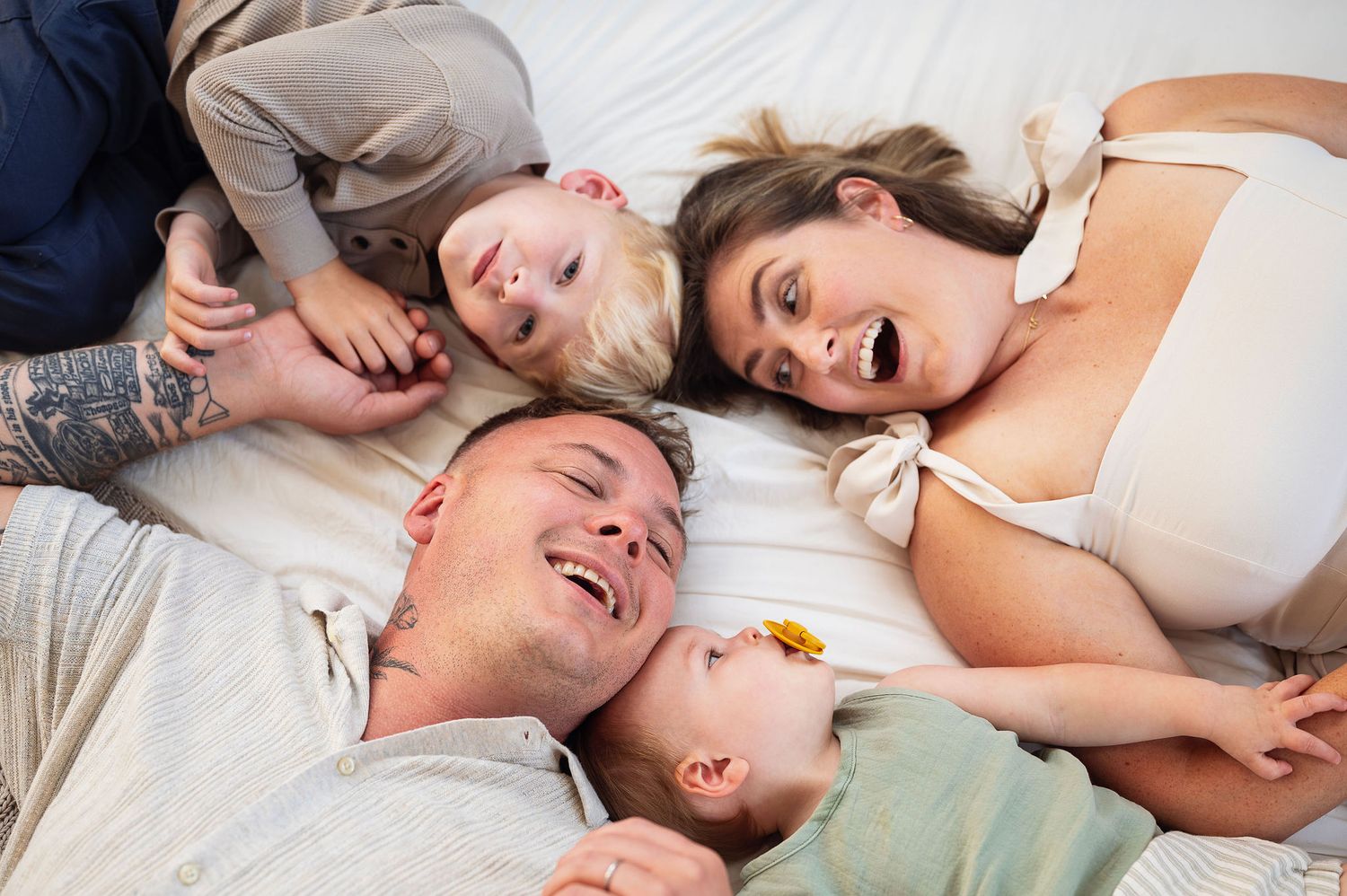 Family laying together on a bed, smiling and relaxed during an in-home lifestyle session in New Albany, Ohio.
