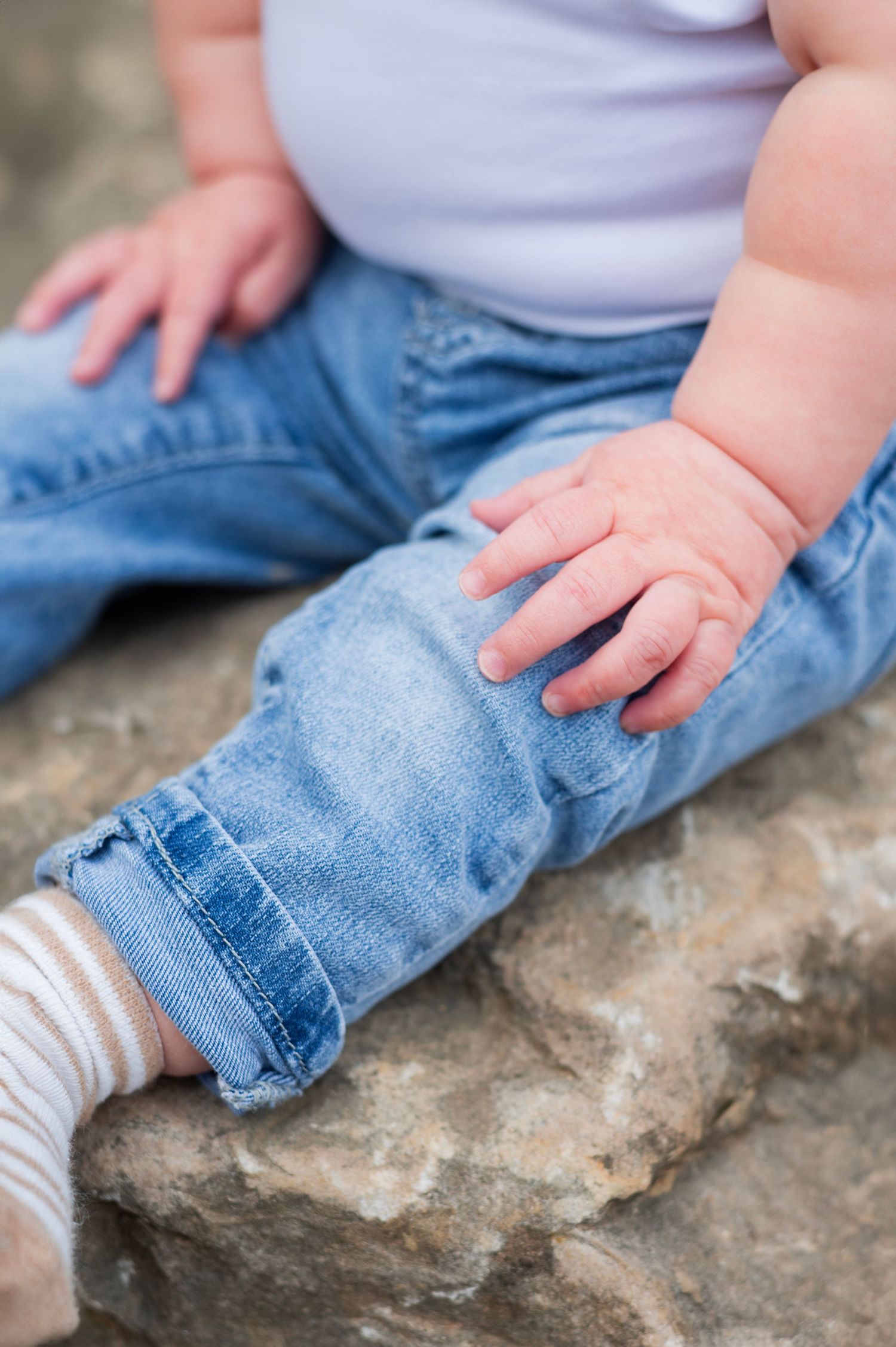 Baby’s chubby hand resting on denim-clad legs, capturing quiet detail.