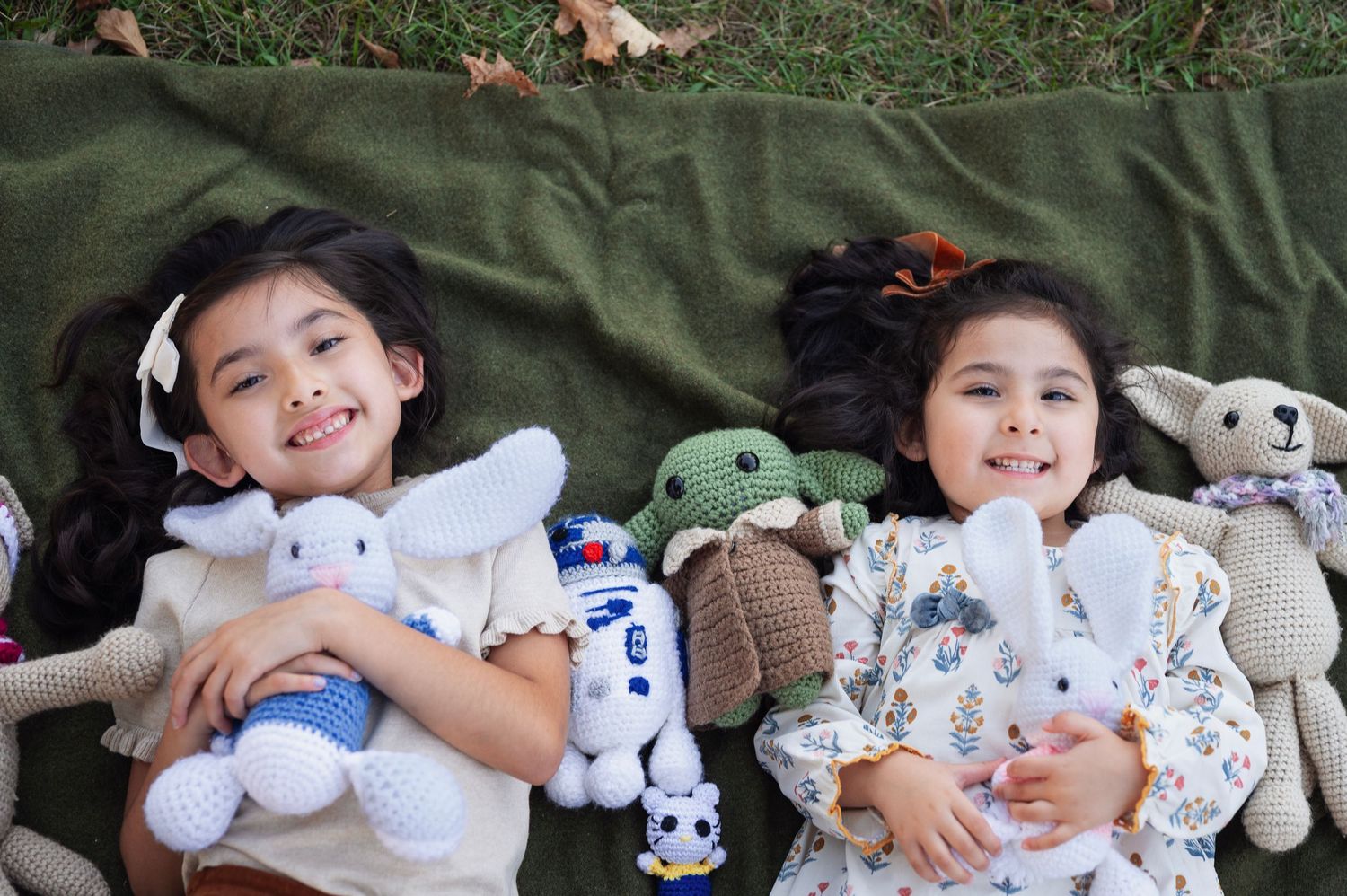 Two sisters lying on a blanket, smiling and cuddling crocheted bunnies and Star Wars stuffies | Westerville family photos.