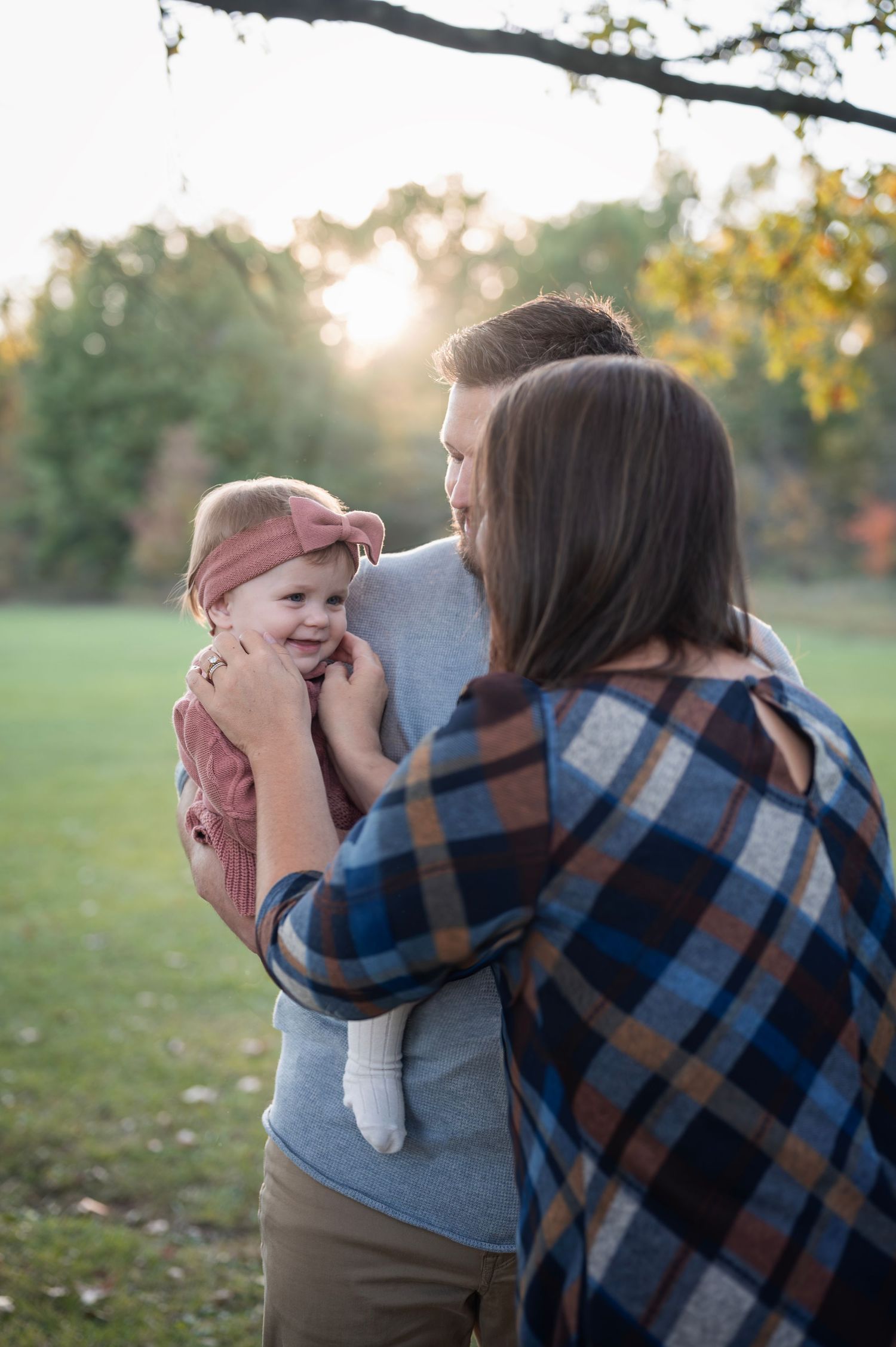 Close-up of parents cuddling their baby during a lifestyle family session, showing cozy textures in a knit romper, headband
