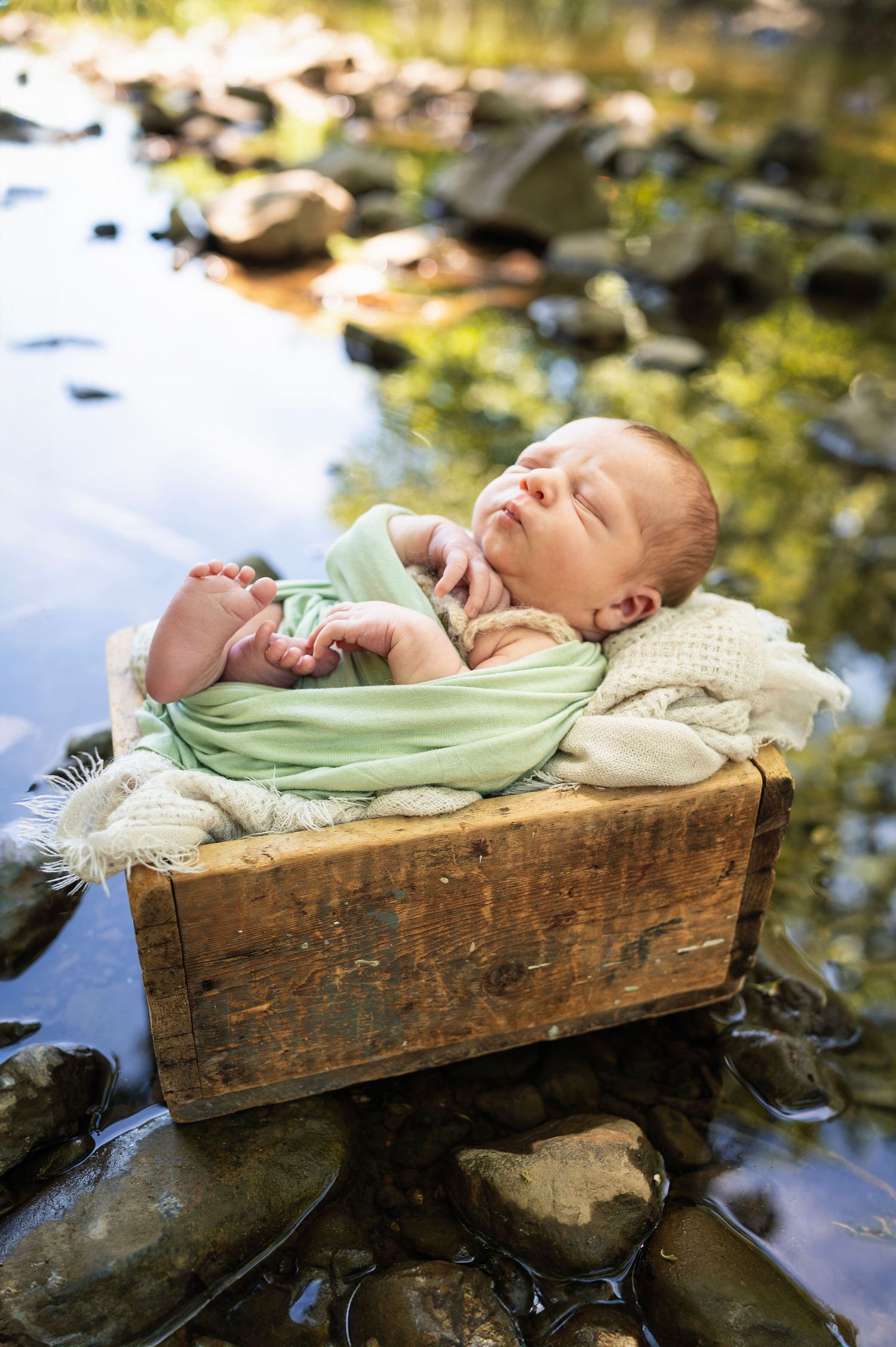 Newborn swaddled in green, sleeping by the water during a nature-inspired newborn session in Gahanna, Ohio.