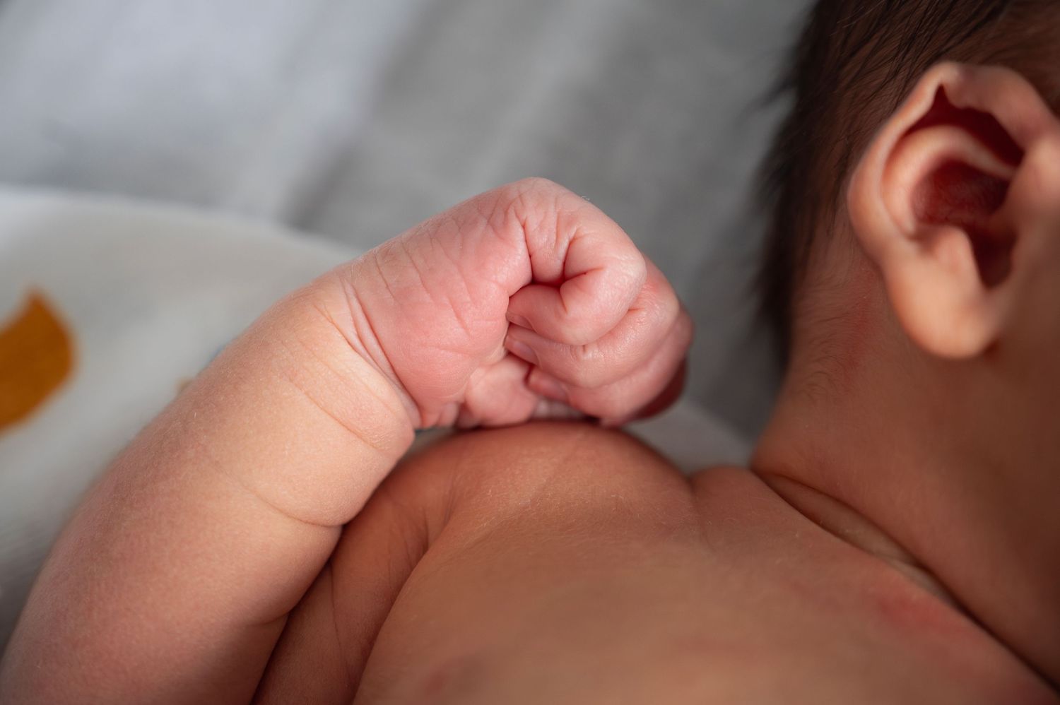Close-up of newborn wrapped in a duck swaddle, highlighting tiny hand and ear in soft light.