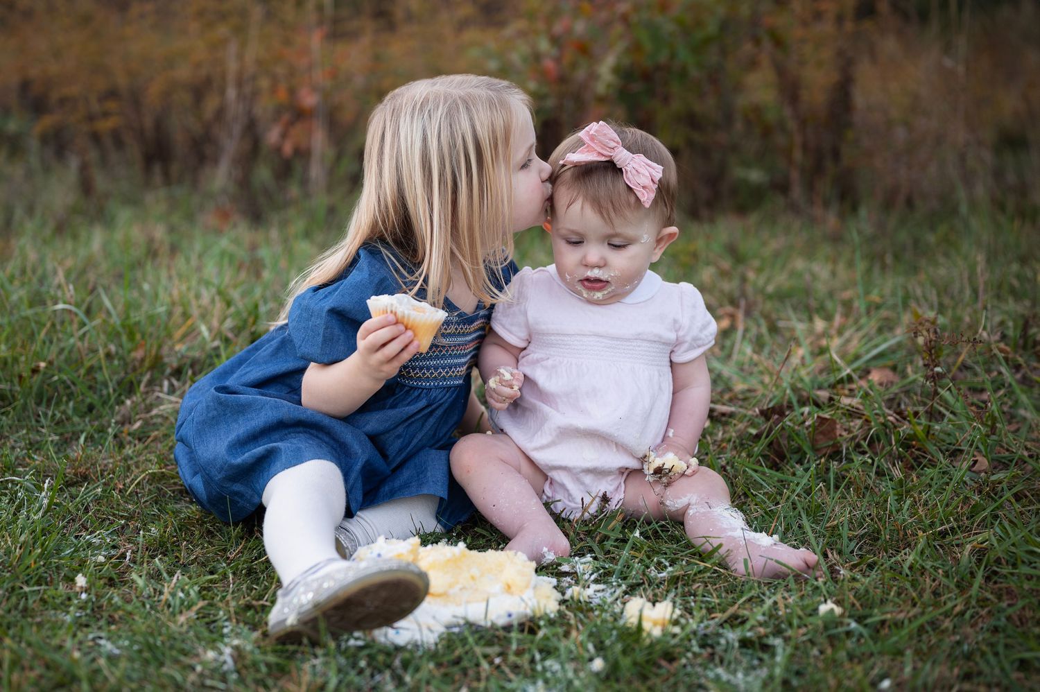 Big sister kissing baby sister during a cake smash in grassy field at Sharon Woods Metro Park