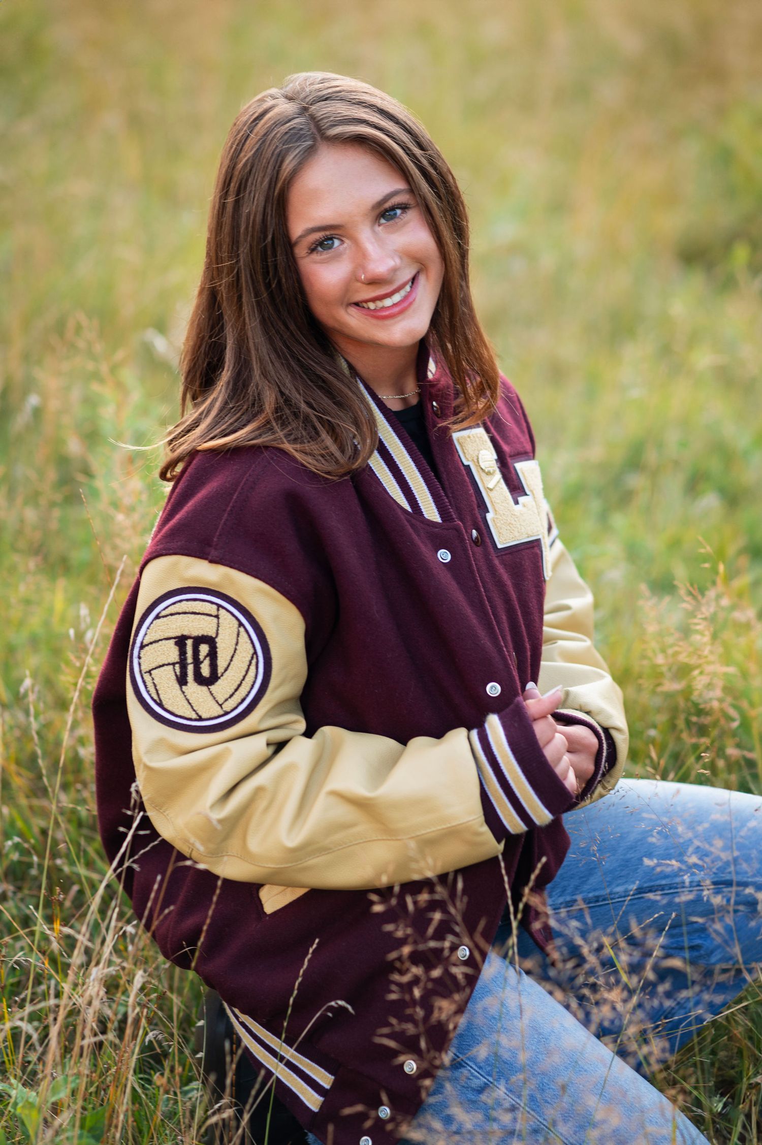 Senior girl in letterman jacket kneeling in a sunlit field at Rocky Fork Metro Park—Westerville senior photographer