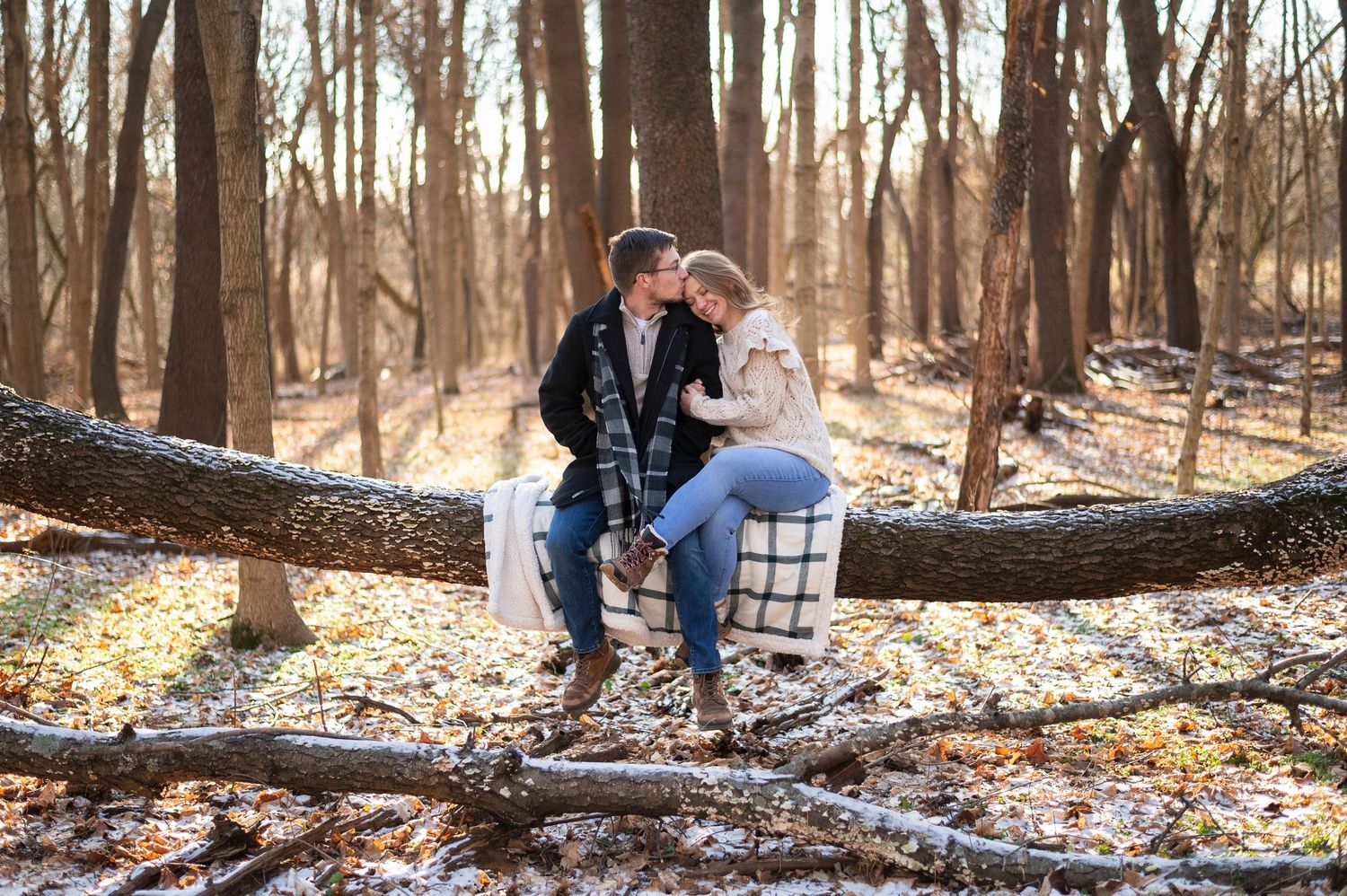 Couple sitting on a log with blanket in snowy woods, cozy winter engagement photo in Columbus.