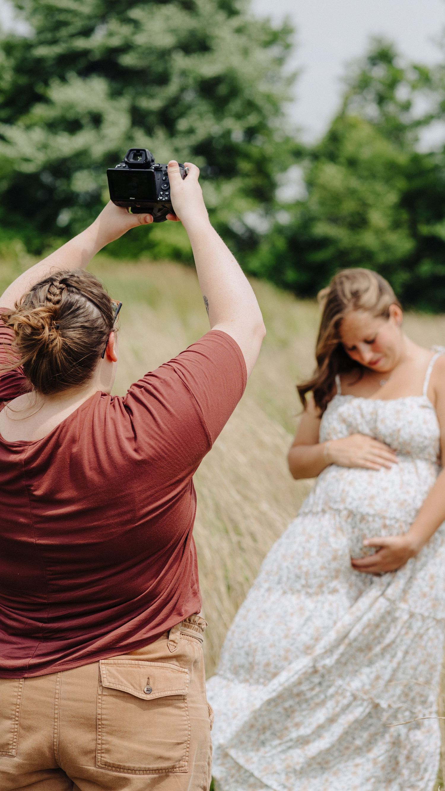 Photographer capturing a maternity session in a grassy field — behind-the-scenes look at Boundless Joy Photography in action.