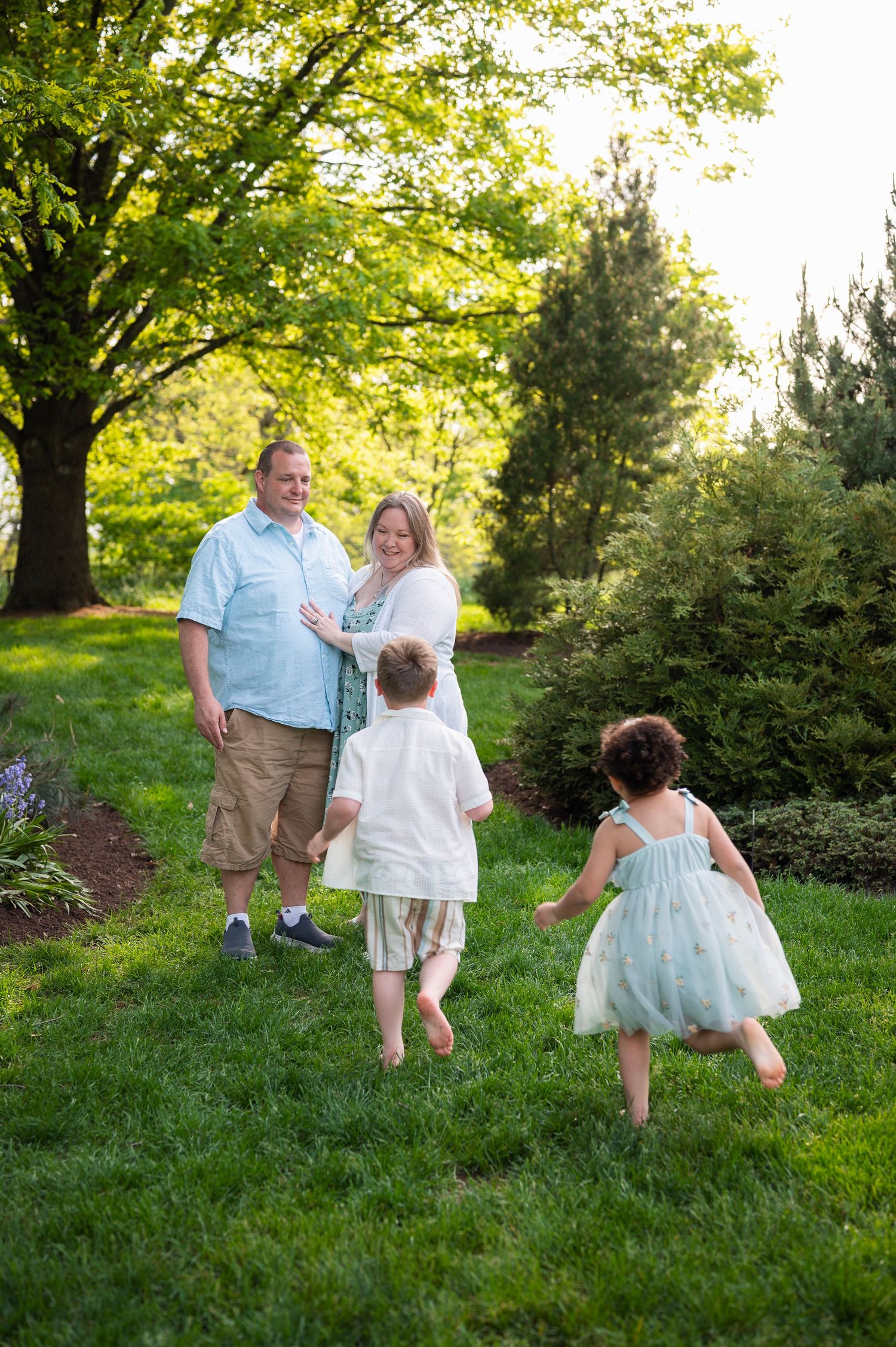 Children running toward parents for joyful, candid family photos in a lush green park setting.