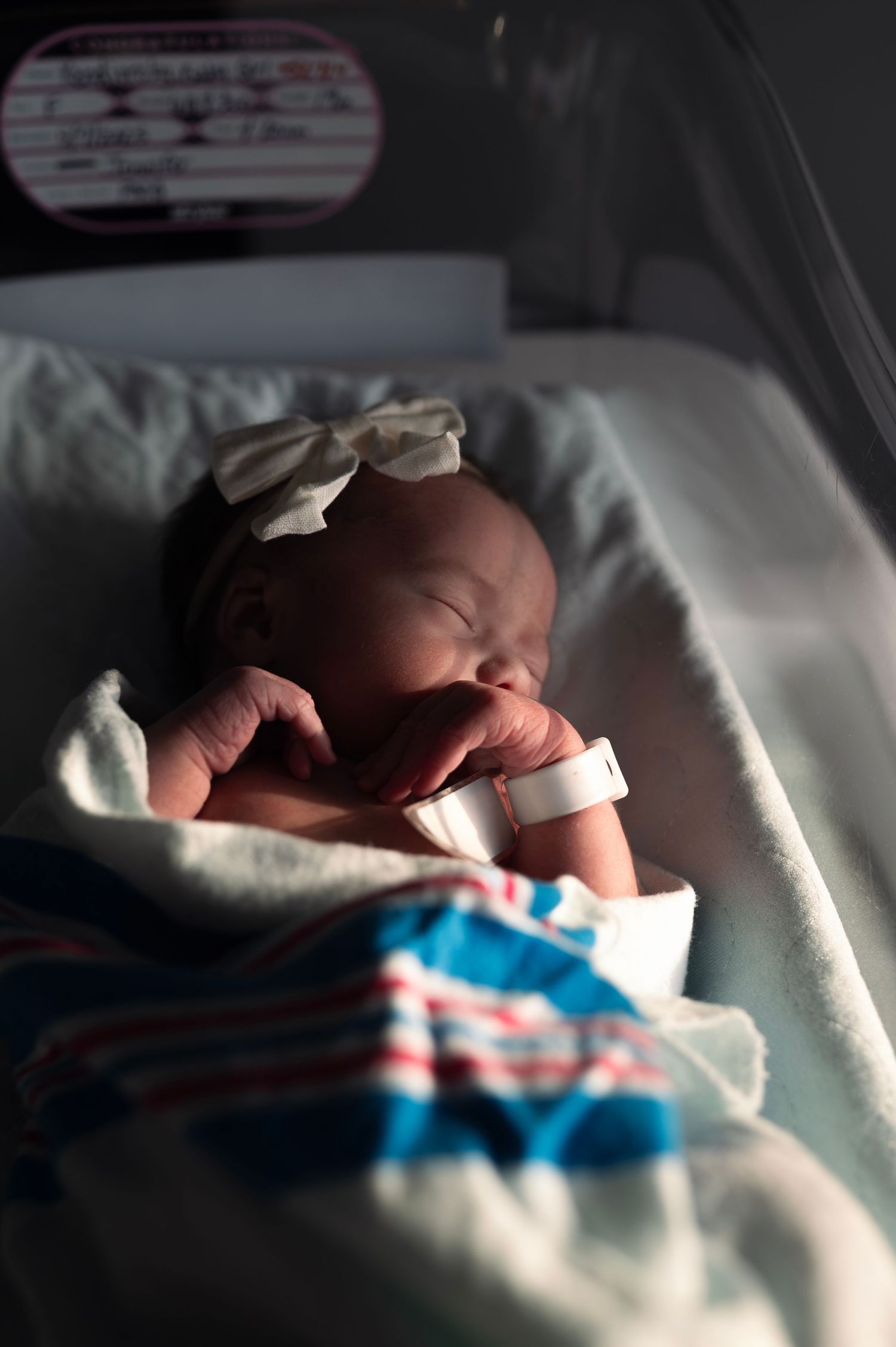Close-up of a newborn boy swaddled in a neutral knit blanket, eyes closed peacefully.